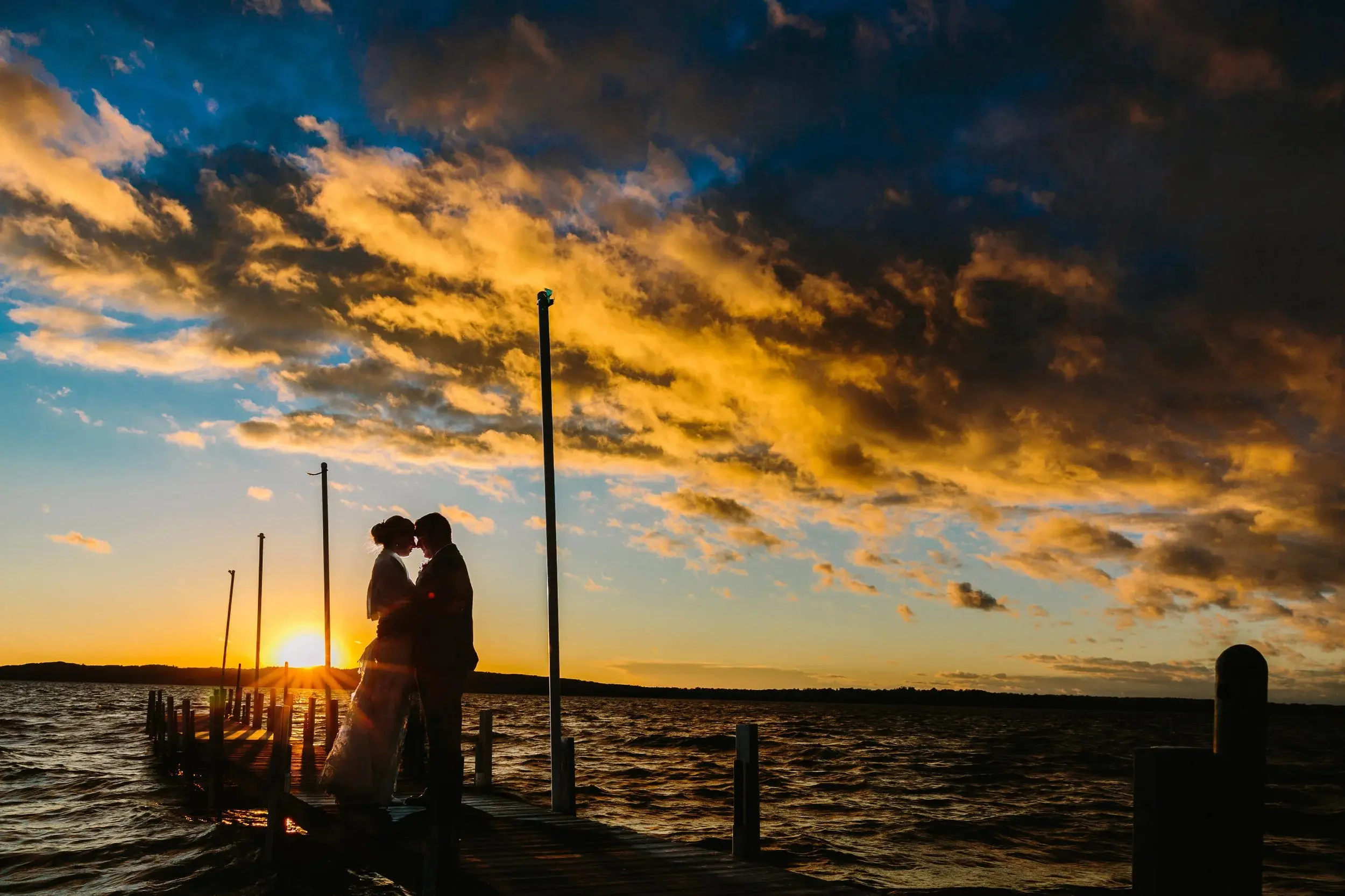 Dock silhouette at golden hour — couple framed by a sky of gold and blue stripes — Tim Larsen Photography, Brainerd Lakes MN