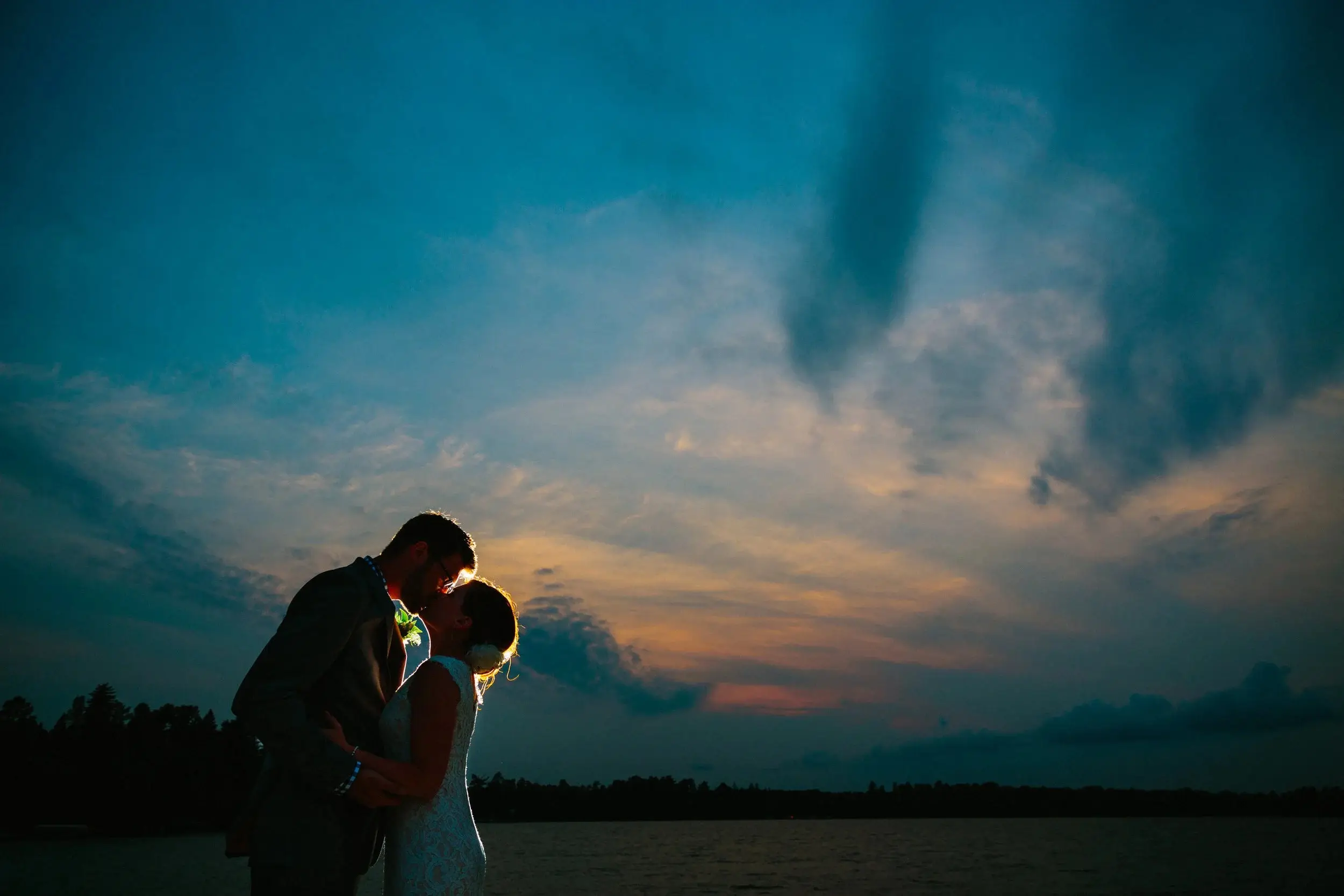 Couple silhouetted kissing against an orange and blue sunset over a lake — Tim Larsen Photography, Brainerd Lakes MN