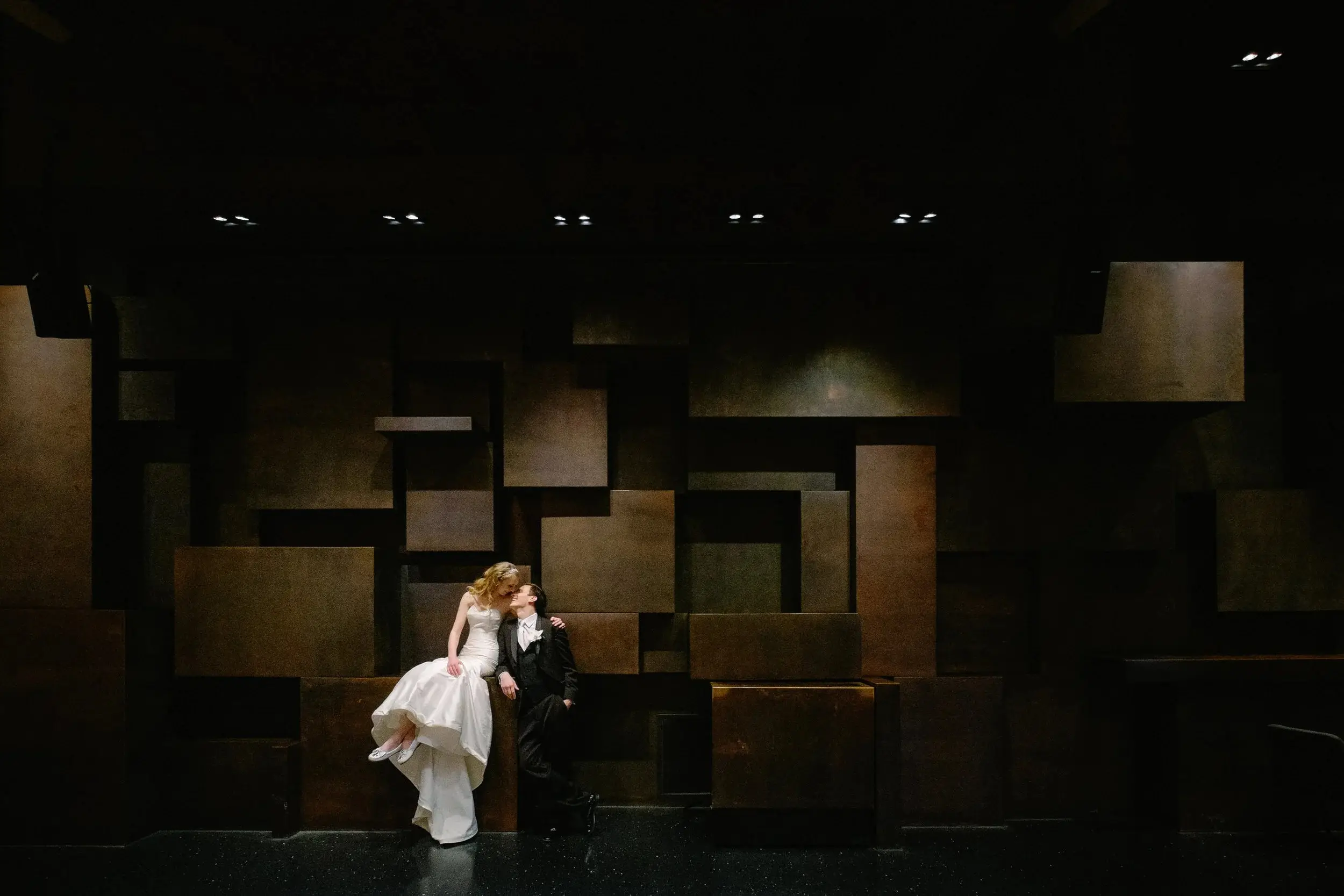 Bride and groom leaning against a rust-colored cubist wall inside a modern reception venue — Tim Larsen Photography, Brainerd Lakes MN