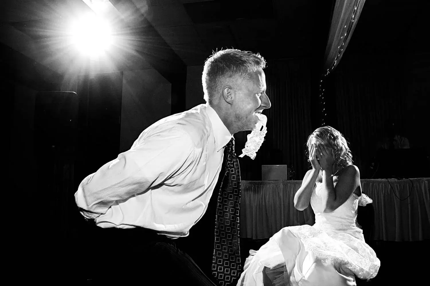 Black-and-white — groom bent forward with the garter in his mouth, bride laughing behind her hands — Tim Larsen Photography, Brainerd Lakes MN