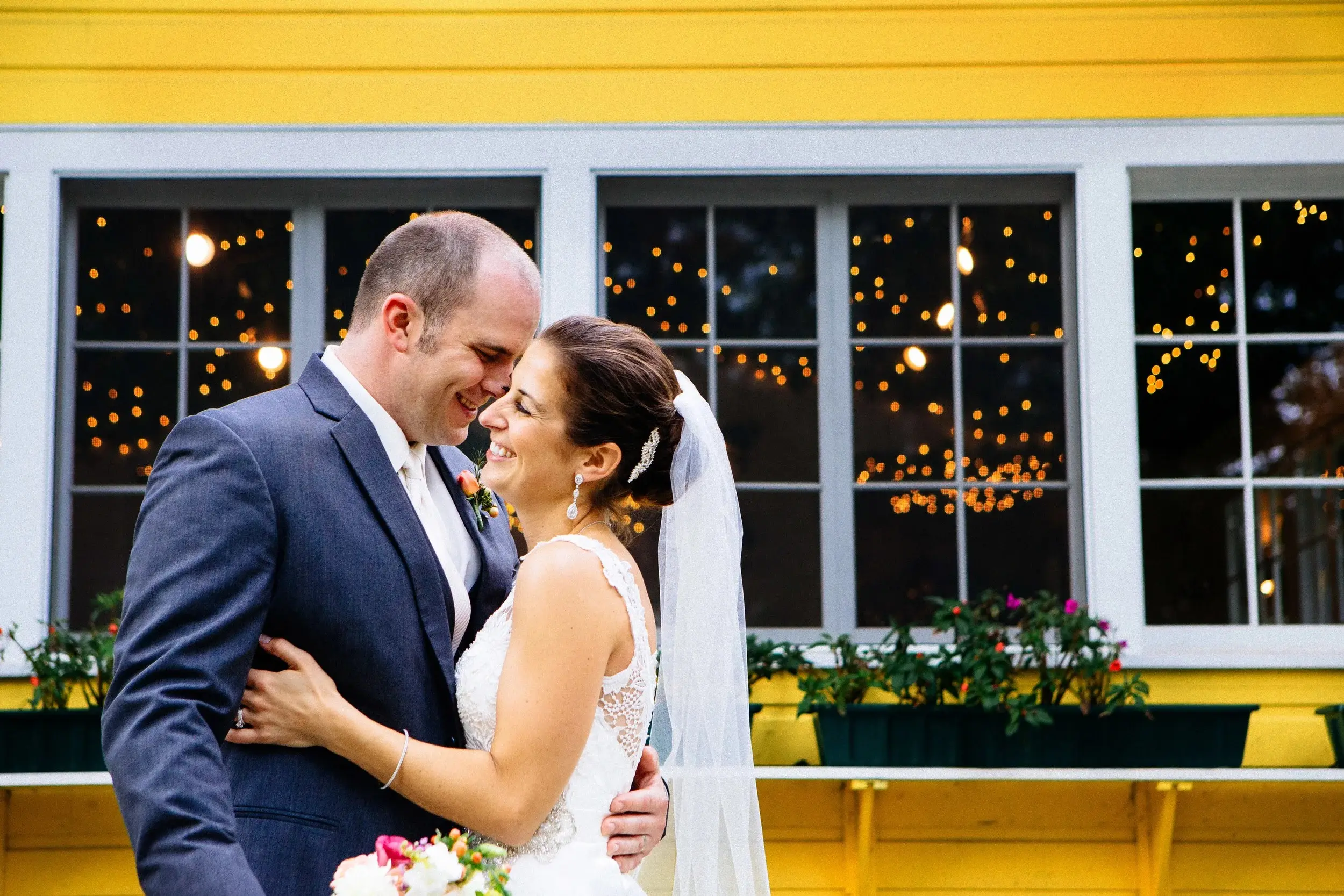 Couple laughing in front of a yellow-painted building, fairy lights in the windows — Tim Larsen Photography, Brainerd Lakes MN