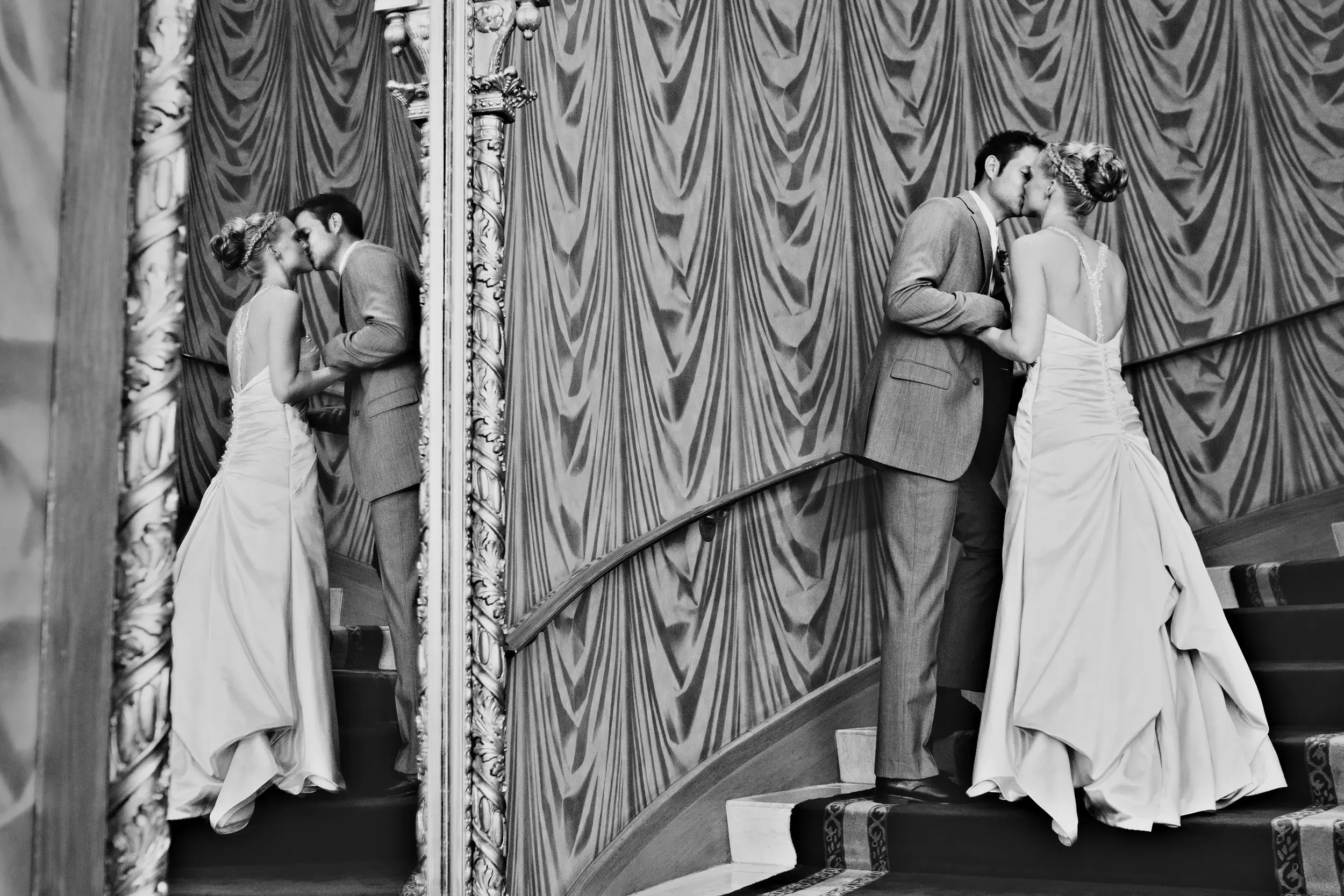 Black-and-white — couple kissing on a grand staircase, a mirror doubling the scene — Tim Larsen Photography, Brainerd Lakes MN