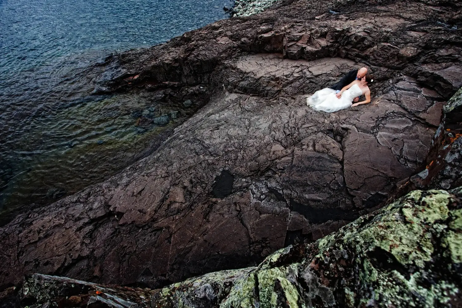 North Shore drama — couple tiny on an expansive rock shelf beside Lake Superior — Tim Larsen Photography, Brainerd Lakes MN