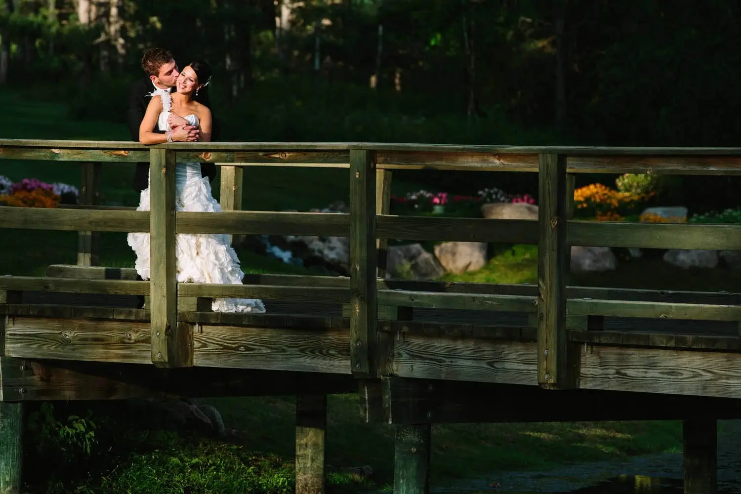 Couple embracing on a wooden footbridge over a garden stream in low afternoon light — Tim Larsen Photography, Brainerd Lakes MN