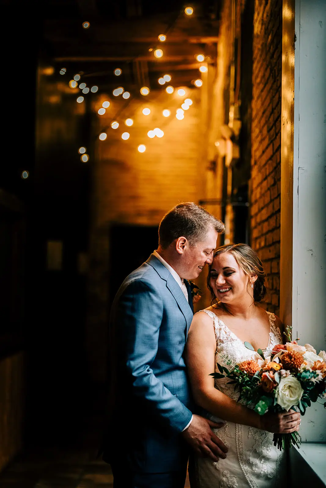 Couple close together in a brick alley strung with warm tungsten string lights — Tim Larsen Photography, Brainerd Lakes MN