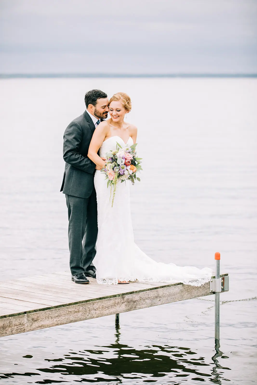 Full-length dock portrait, bride holding a soft pastel bouquet over still lake water — Tim Larsen Photography, Brainerd Lakes MN