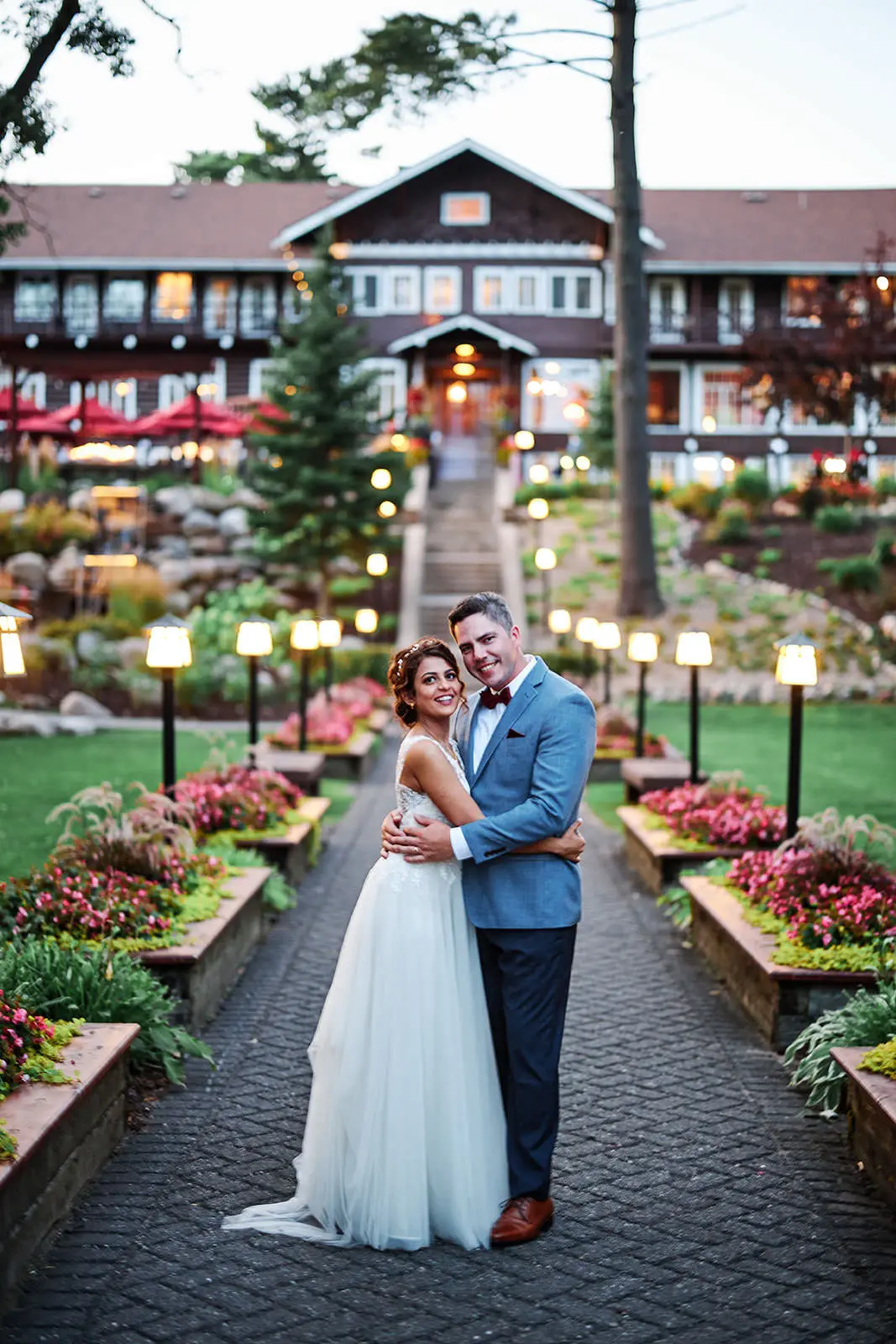 Couple embracing on a lantern-lit garden path to a historic lodge at dusk — Tim Larsen Photography, Brainerd Lakes MN