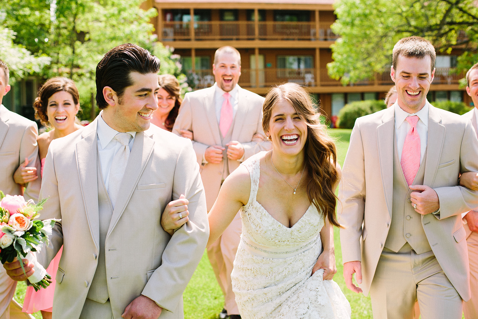 Couple laughing with wedding party in pink ties and tan suits on the resort grounds — Tim Larsen Photography, Brainerd Lakes MN