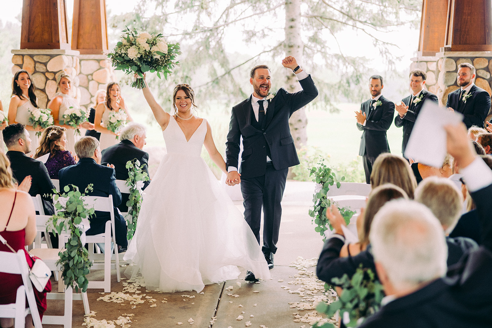 Couple raising hands after ceremony in the Antlers Pavilion — stone fireplace and greenery — Tim Larsen Photography, Brainerd Lakes MN