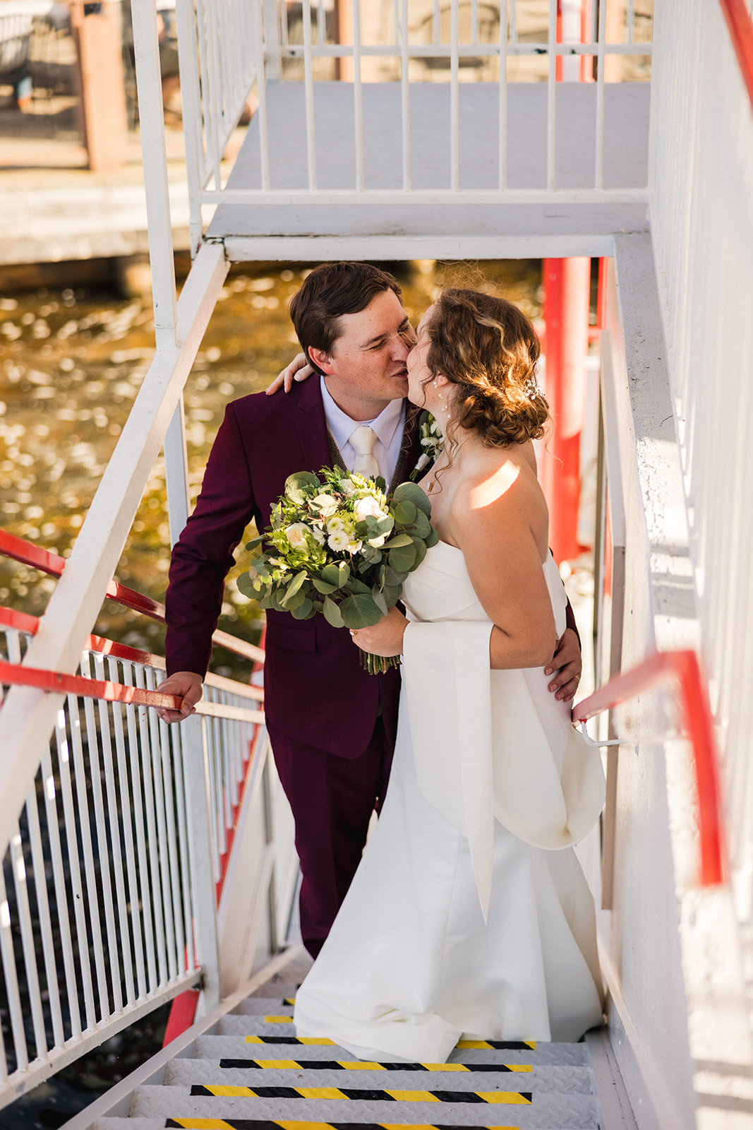 Couple kissing on the gangway of the Breezy Belle steamboat — burgundy suit — Tim Larsen Photography, Brainerd Lakes MN