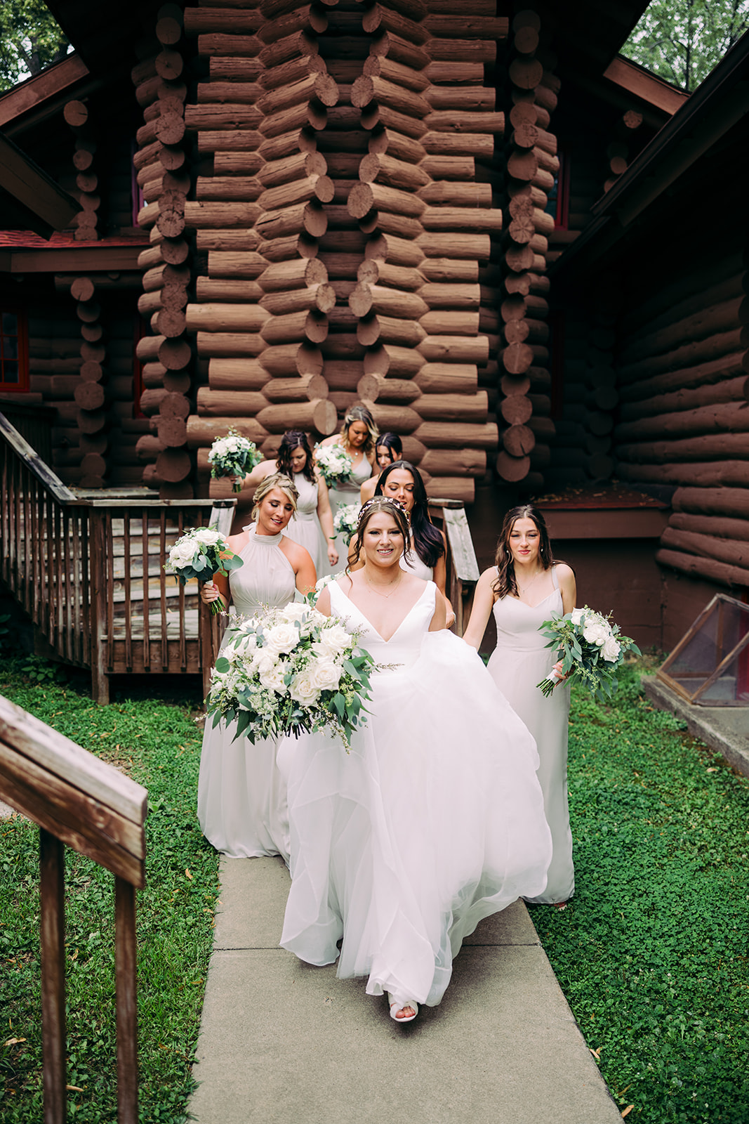 Bride with bridesmaids in white dresses walking from the log cabin chapel — Tim Larsen Photography, Brainerd Lakes MN