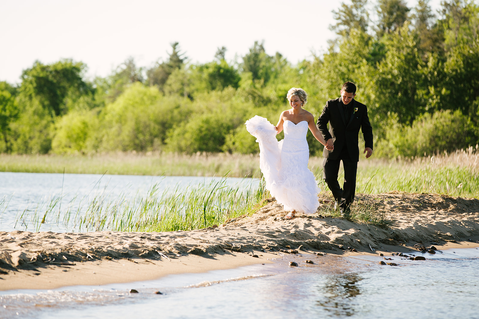 Couple walking on the beach at golden hour — bride holding dress up — Tim Larsen Photography, Brainerd Lakes MN