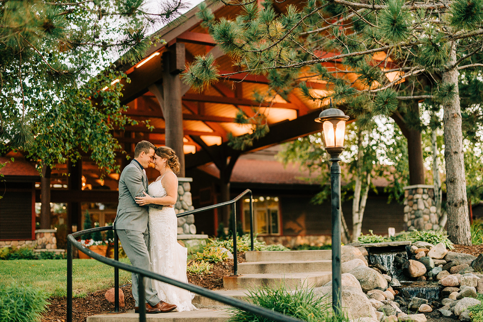 Couple kissing on the walkway by the timber-frame lodge entrance at golden hour — Tim Larsen Photography, Brainerd Lakes MN