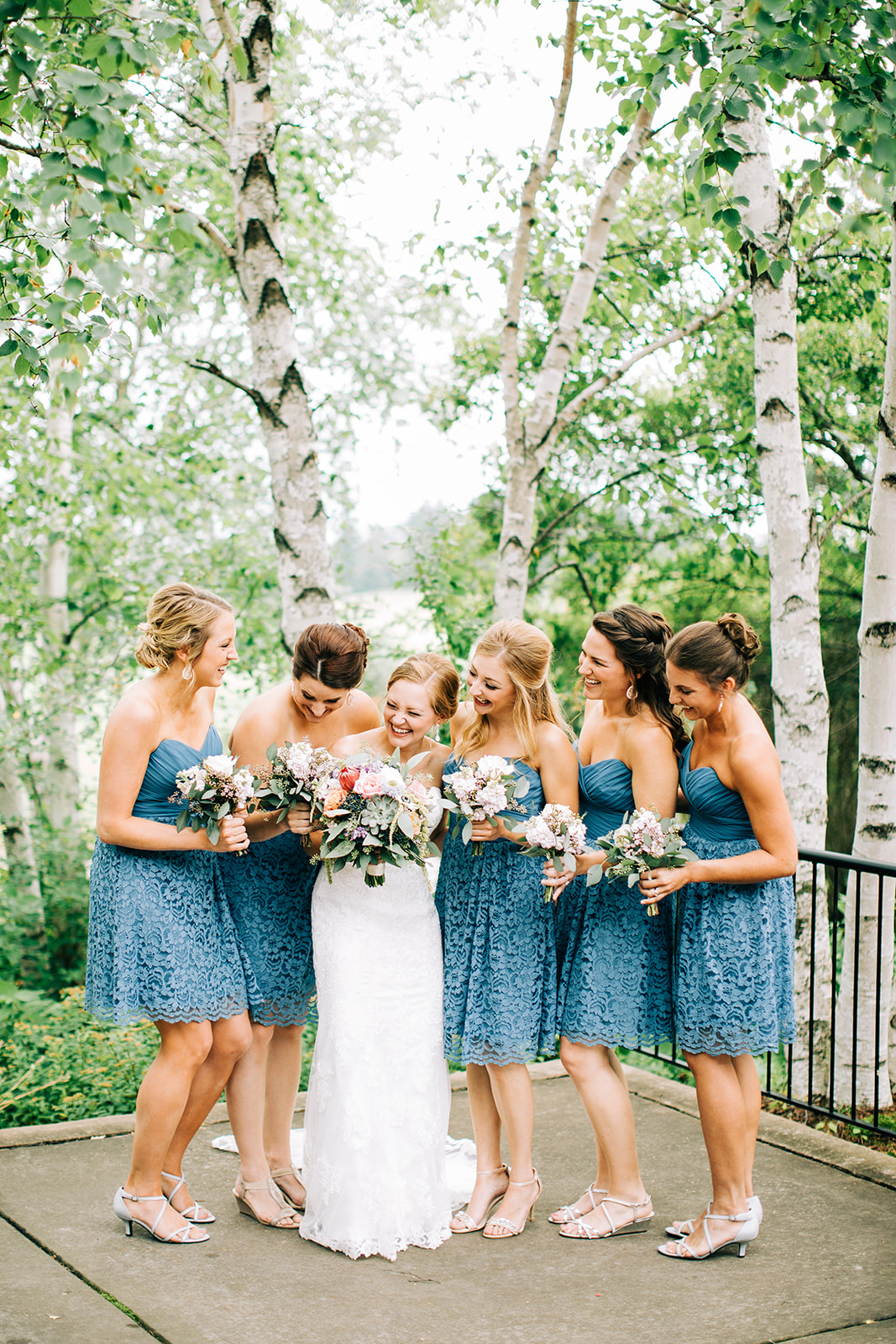 Bride laughing with bridesmaids in blue lace dresses under birch trees — Tim Larsen Photography, Brainerd Lakes MN