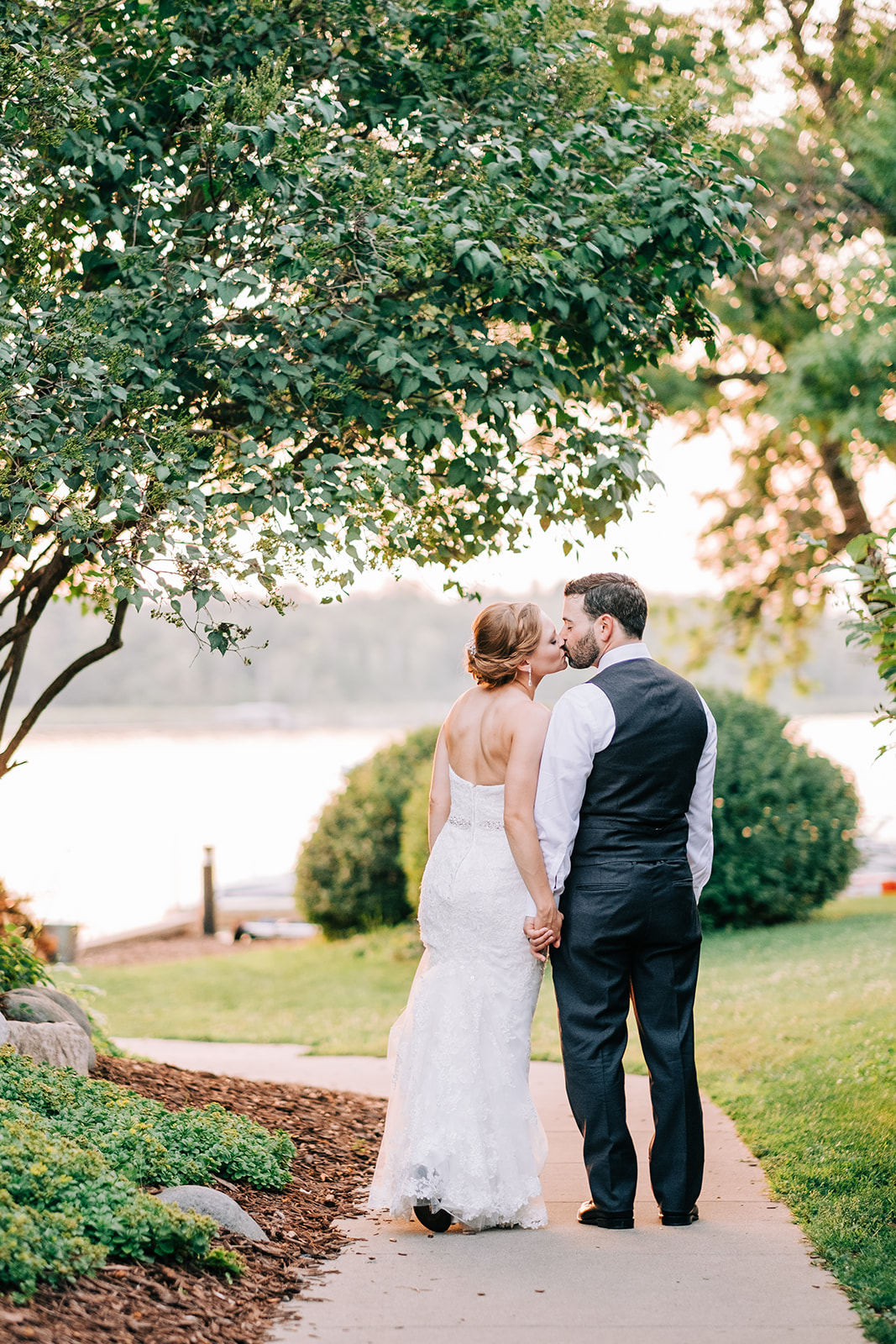 Couple kissing on the tree-lined path at sunset — backs to camera, holding hands — Tim Larsen Photography, Brainerd Lakes MN