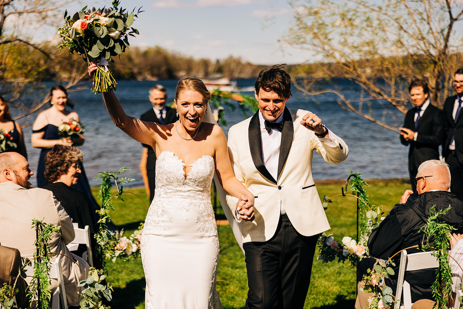 Recessional celebration — bride with bouquet raised, groom fist pumping, lakeside ceremony — Tim Larsen Photography, Brainerd Lakes MN