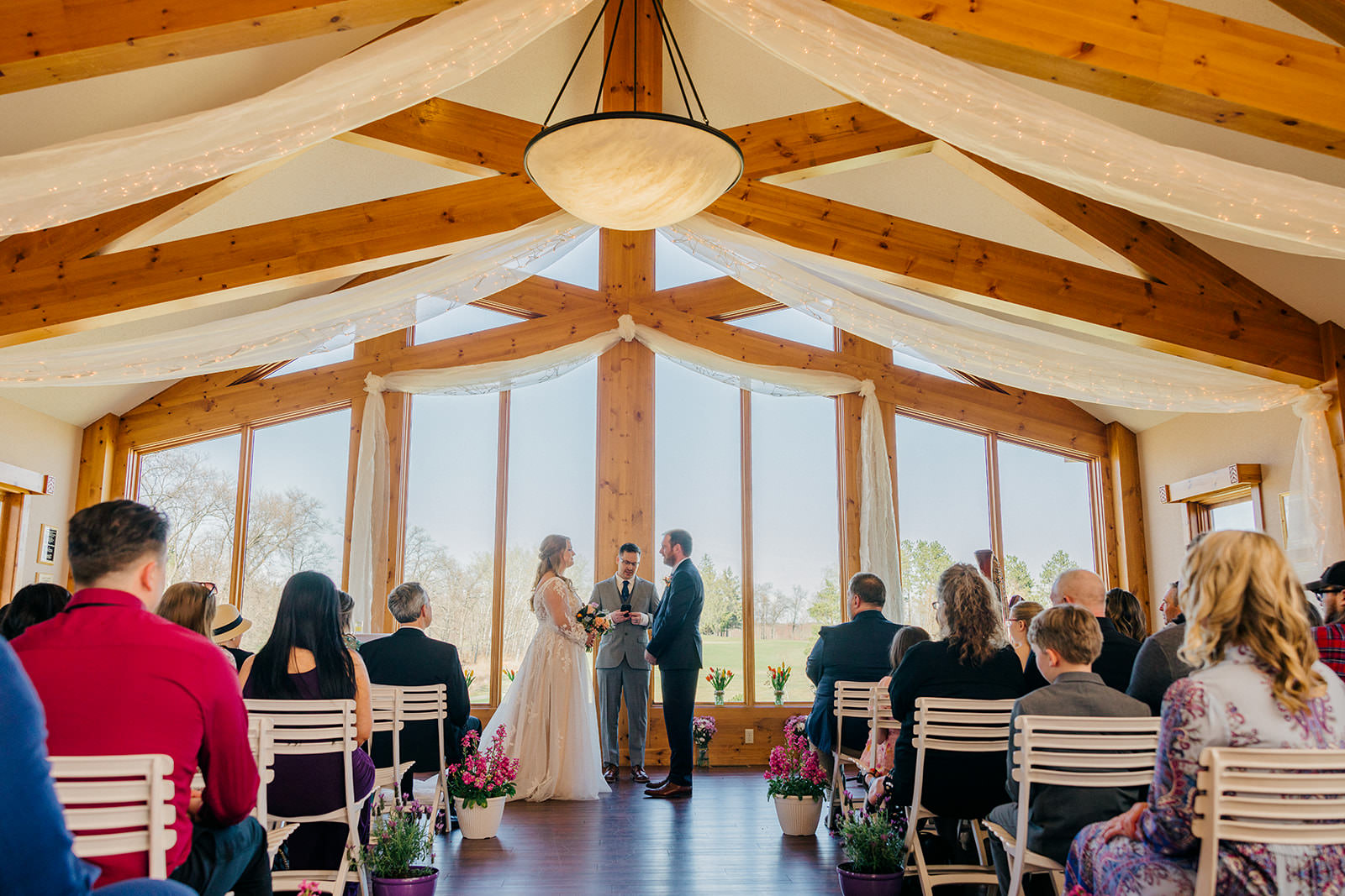 Indoor ceremony at the Legacy Pavilion — timber beams, draping, lake views through windows — Tim Larsen Photography, Brainerd Lakes MN