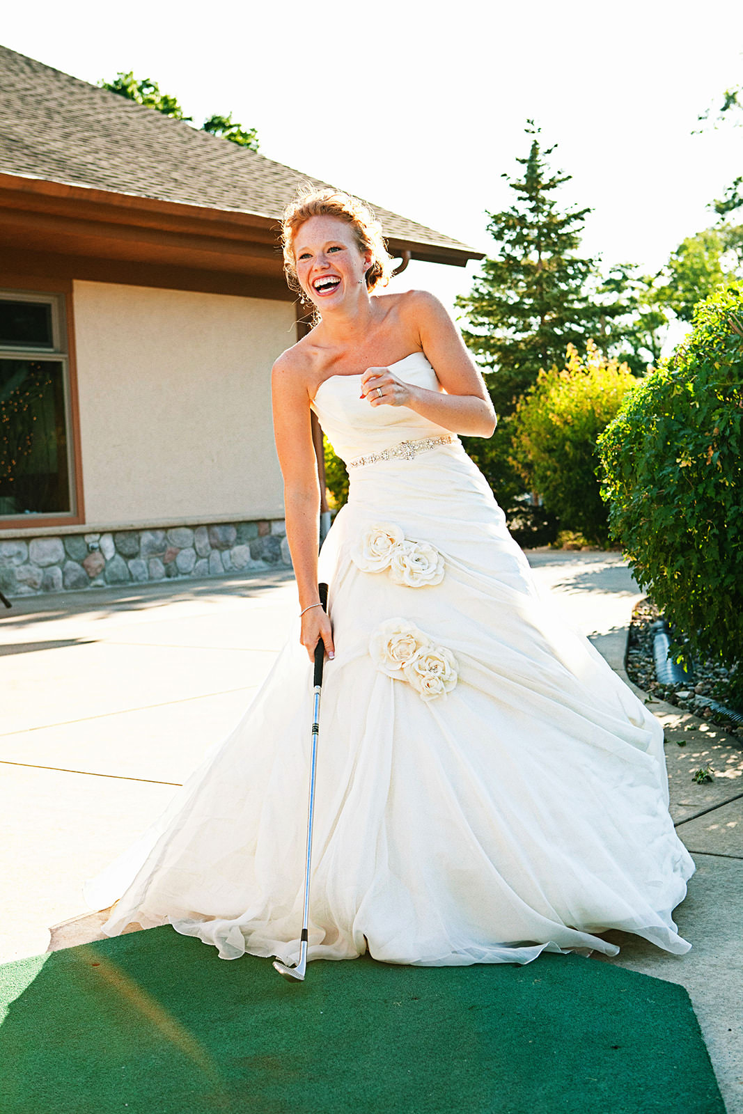 Bride laughing with golf club in her wedding dress — clubhouse patio — Tim Larsen Photography, Brainerd Lakes MN