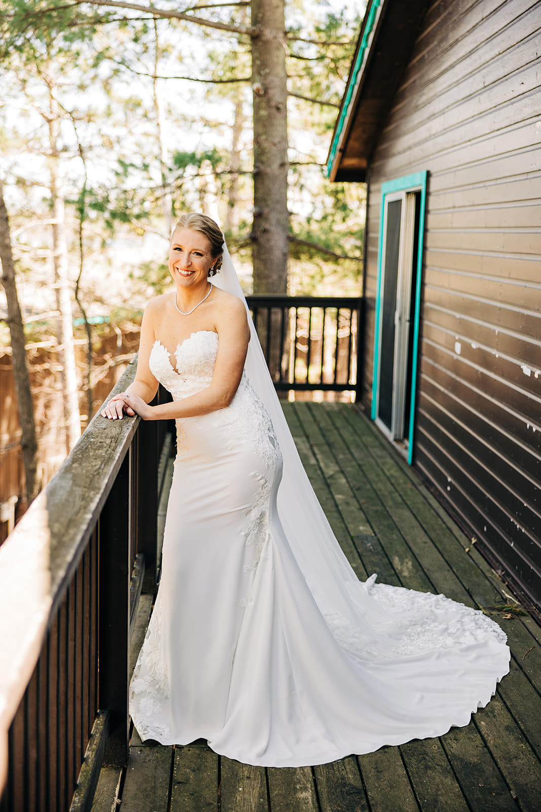 Bride on the cabin deck — morning light through the pines, long train — Tim Larsen Photography, Brainerd Lakes MN