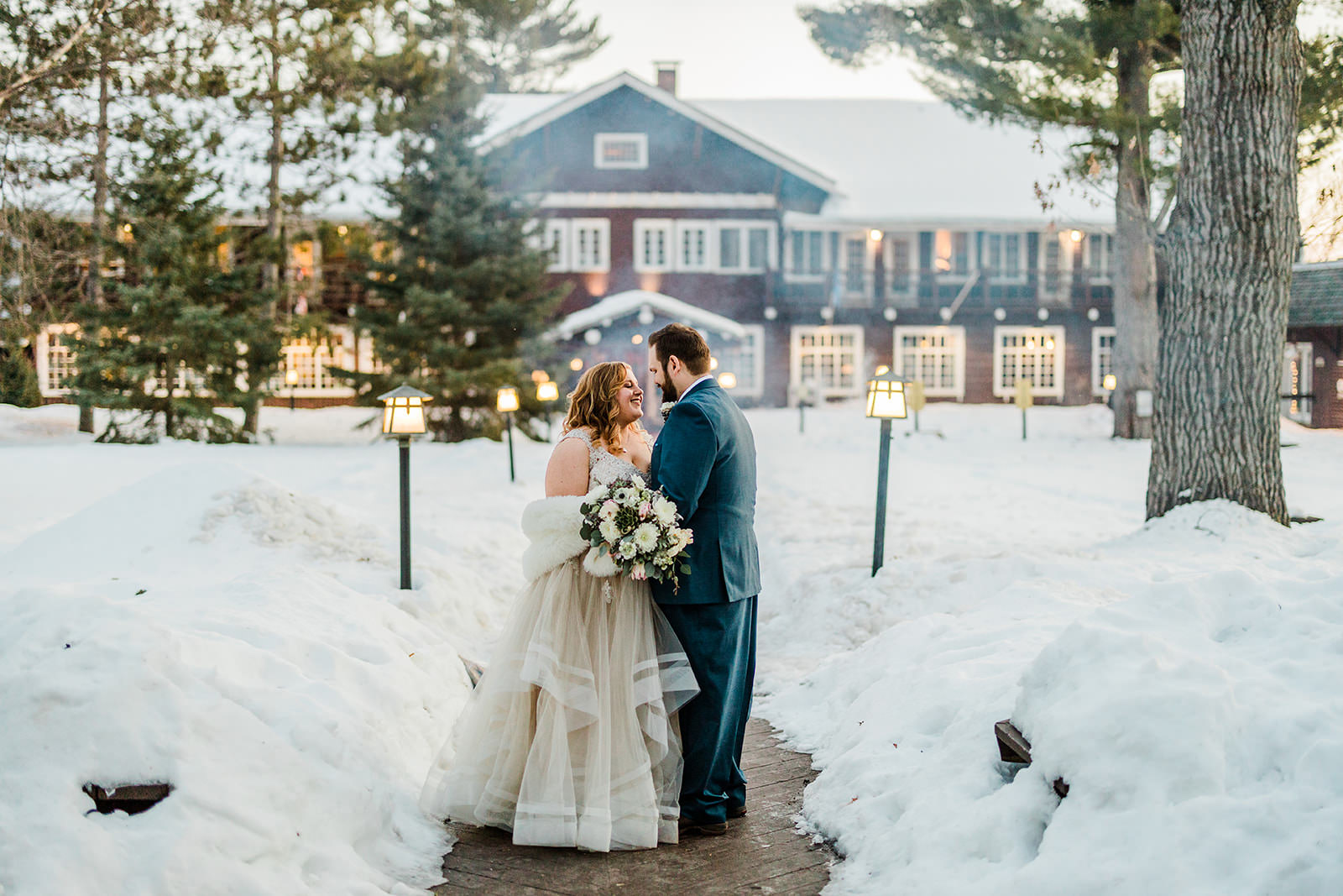 Winter wedding portrait — couple on the snowy path with the lodge behind — Tim Larsen Photography, Brainerd Lakes MN