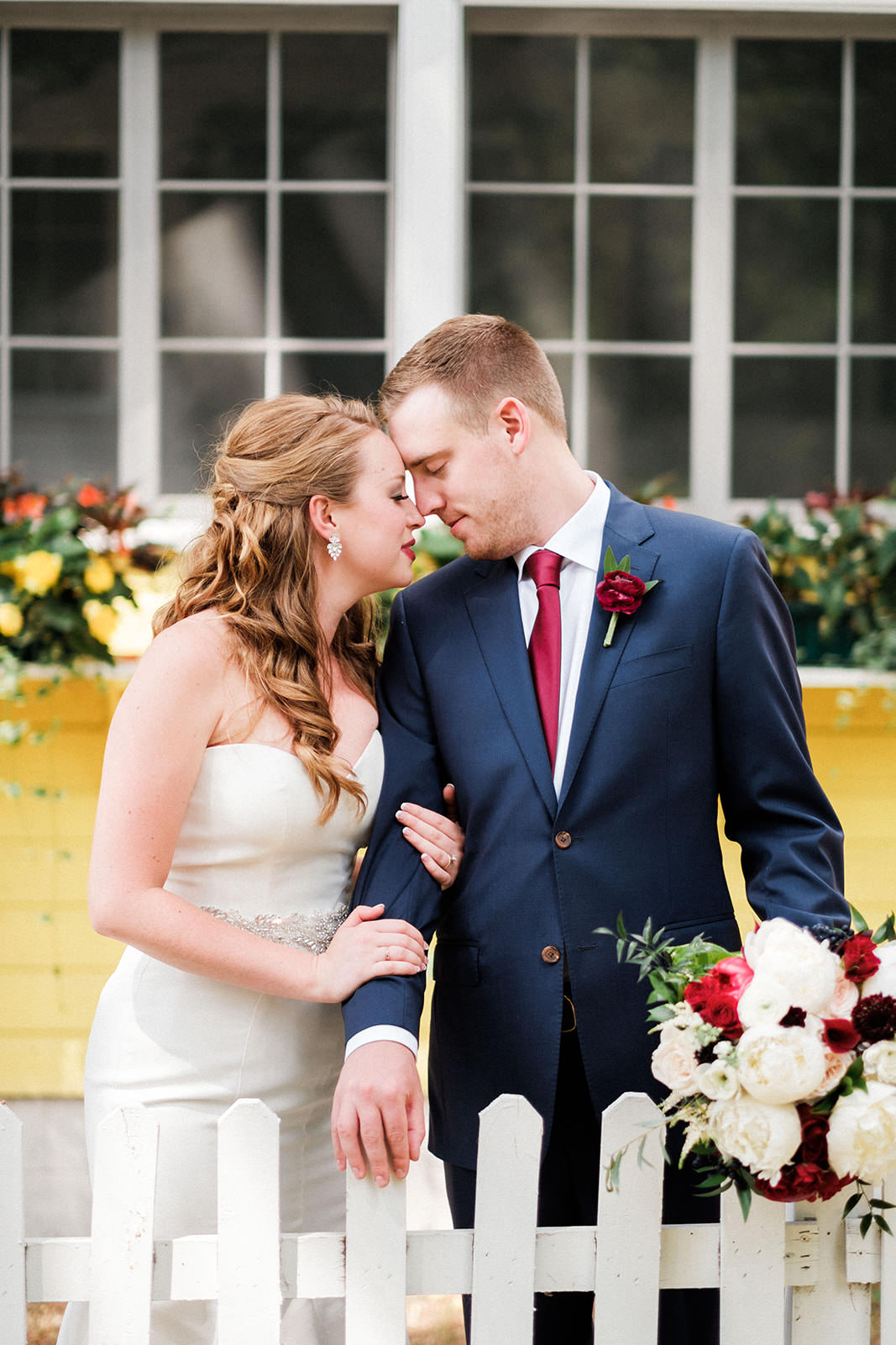 Couple portrait by the white picket fence with red and white bouquet — Tim Larsen Photography, Brainerd Lakes MN