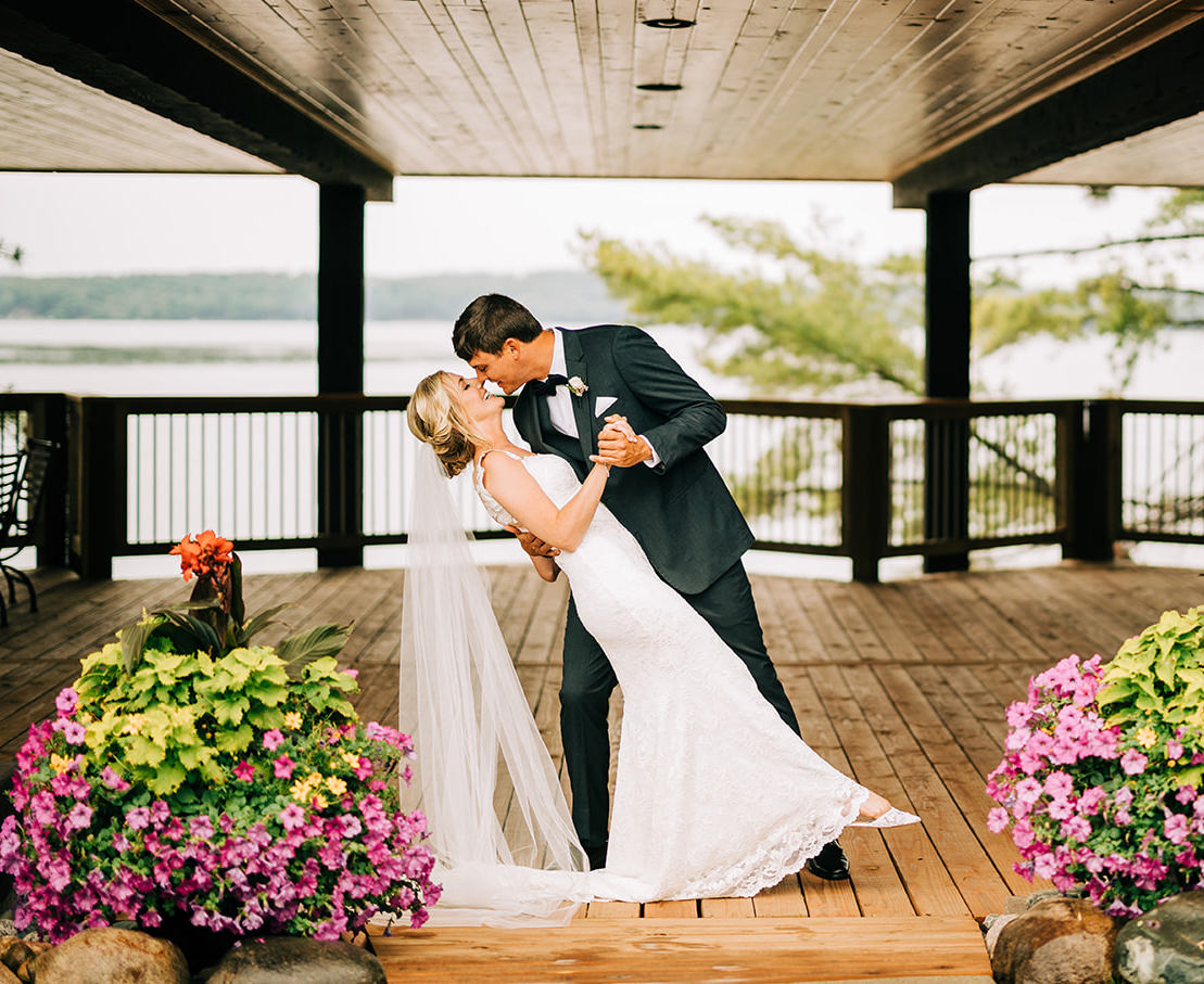Couple dip kiss on the covered deck — lake and flowers in the background — Tim Larsen Photography, Brainerd Lakes MN