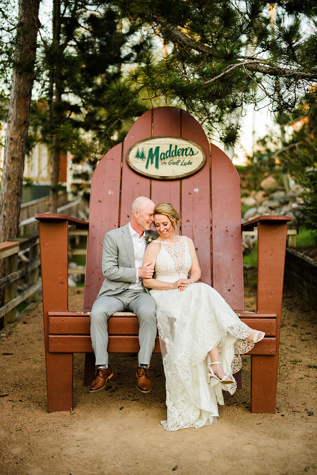 Couple sitting in the oversized Madden's chair — pine trees and resort sign — Tim Larsen Photography, Brainerd Lakes MN