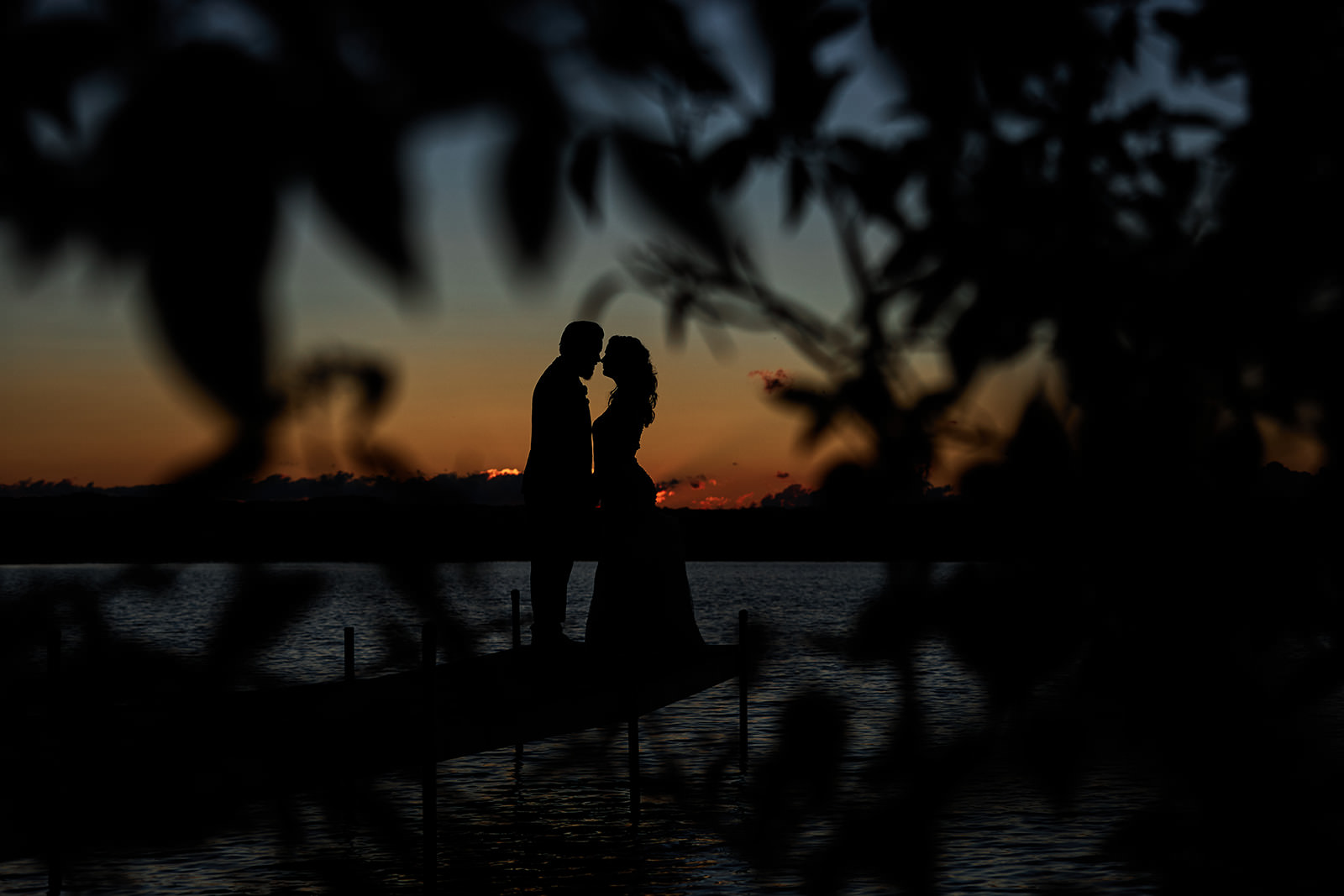 Couple silhouette on the dock at sunset — orange sky through tree branches over Gull Lake — Tim Larsen Photography, Brainerd Lakes MN