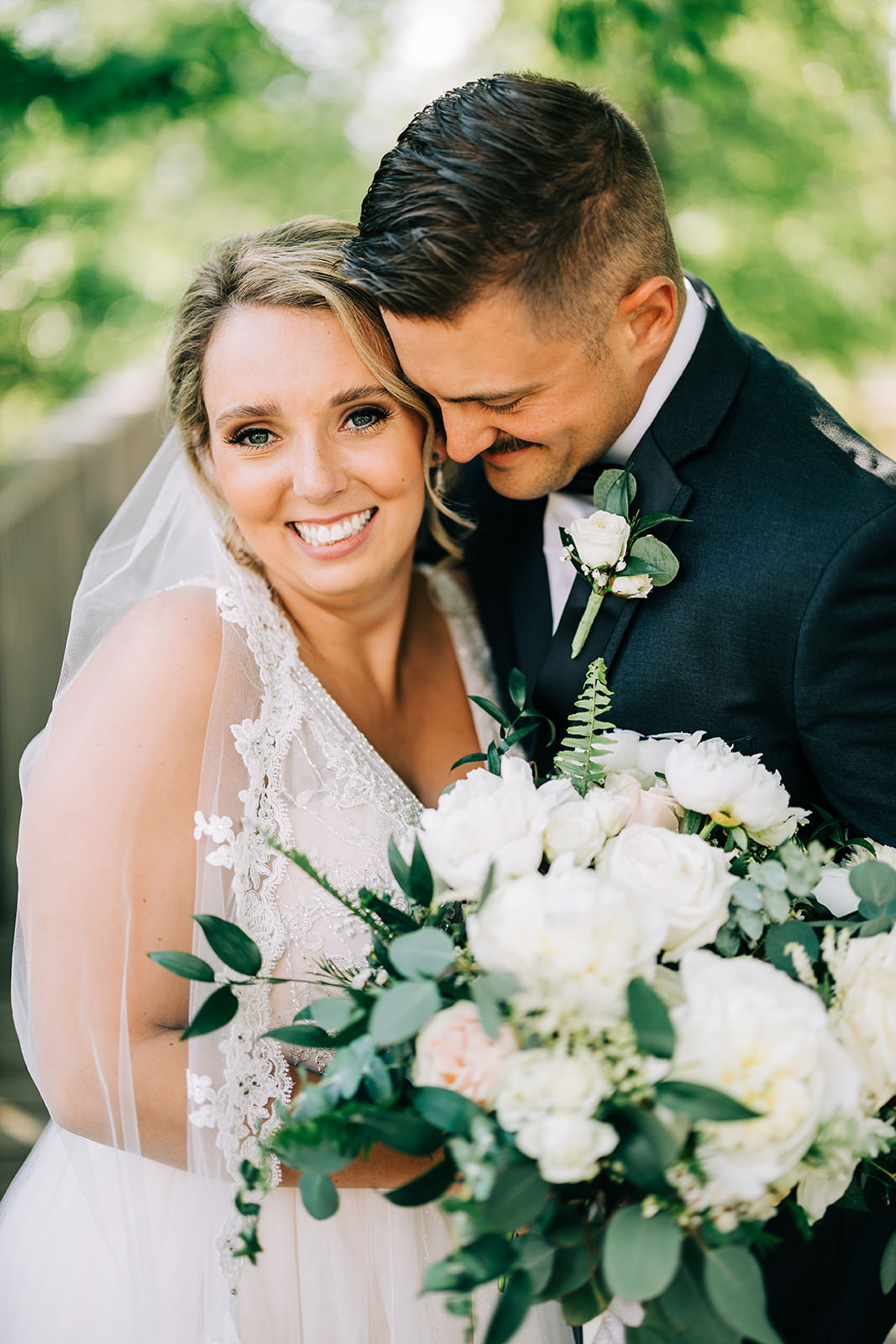 Bride smiling with groom nuzzled close — white peony bouquet with greenery — Tim Larsen Photography, Brainerd Lakes MN