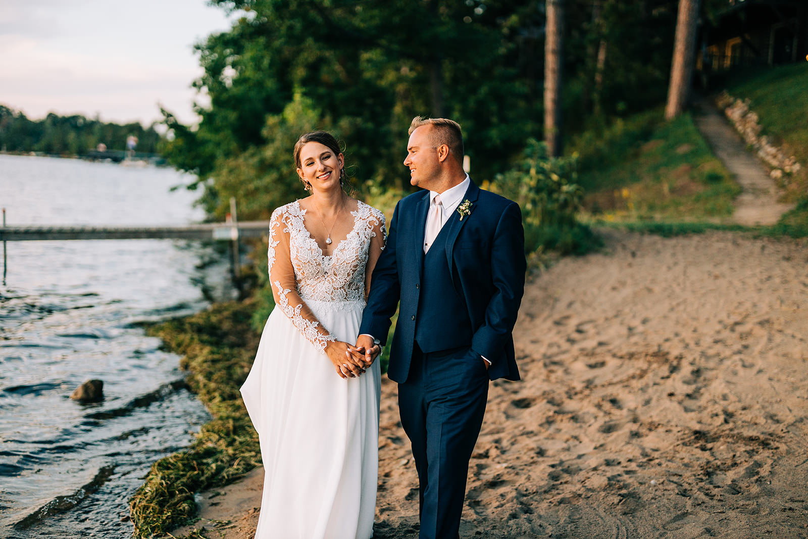 Couple walking on the beach at golden hour — lace sleeves and navy suit — Tim Larsen Photography, Brainerd Lakes MN