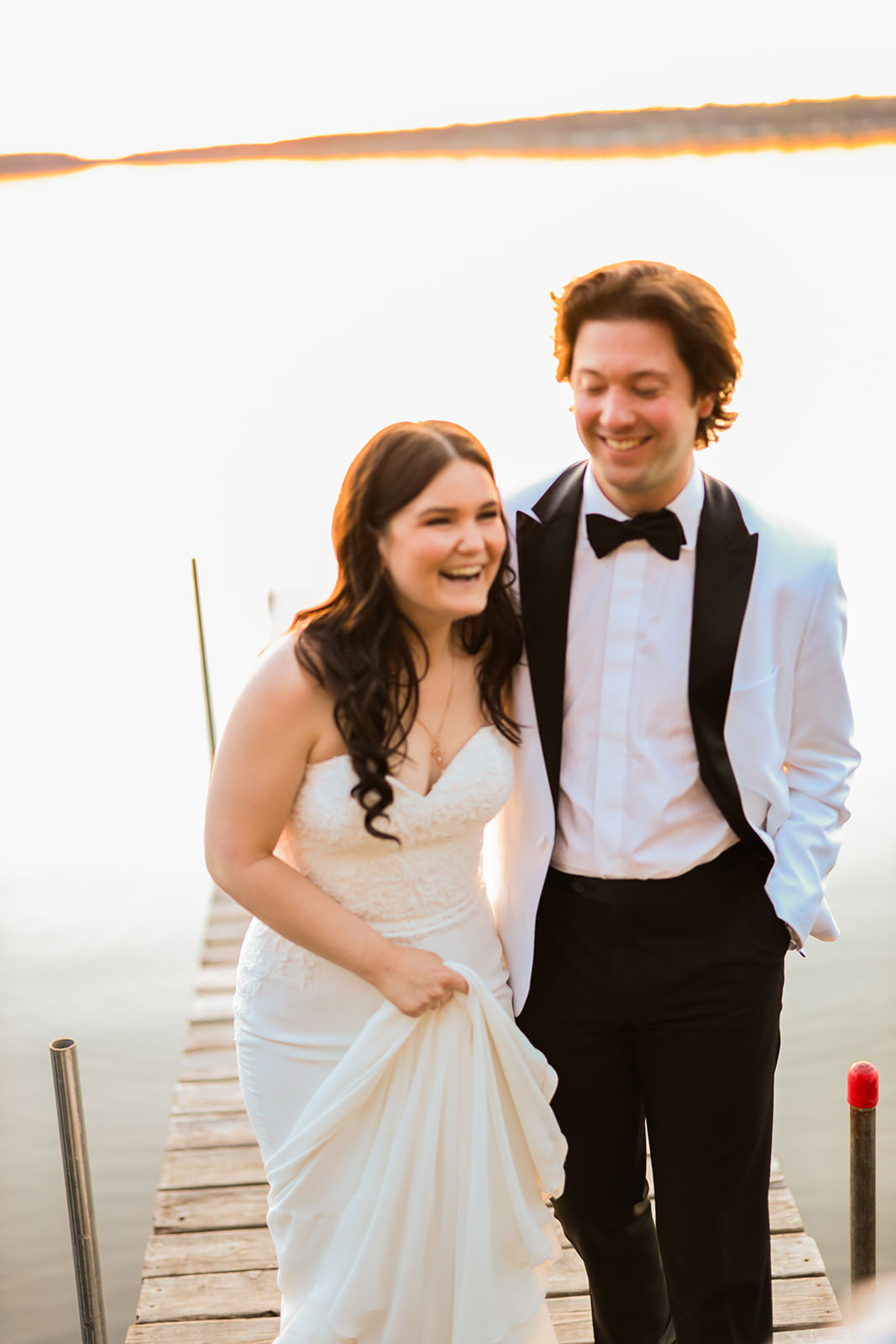 Couple laughing walking down the dock at golden hour — white tux jacket and sweetheart gown — Tim Larsen Photography, Brainerd Lakes MN
