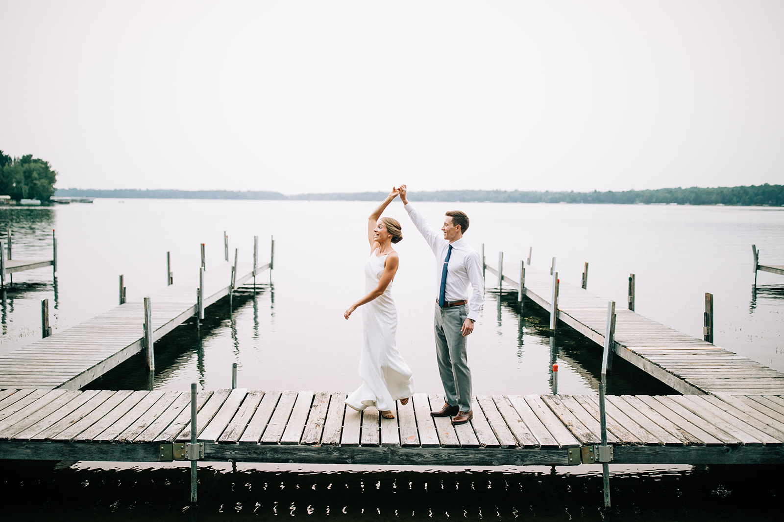 Couple spinning on the dock with the lake stretching behind them — Tim Larsen Photography, Brainerd Lakes MN