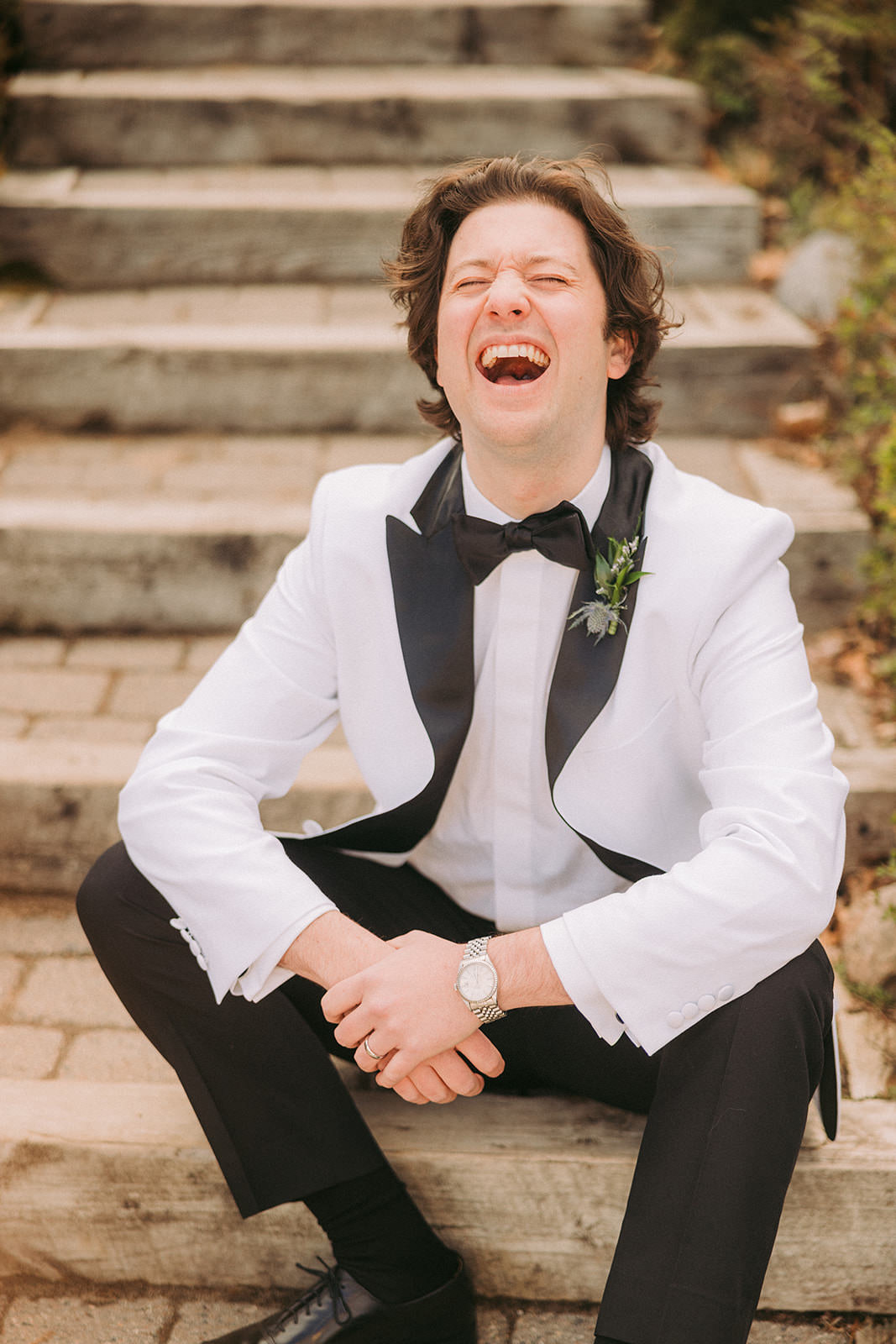 Groom laughing on the stone steps in a white tux jacket and bow tie — Tim Larsen Photography, Brainerd Lakes MN
