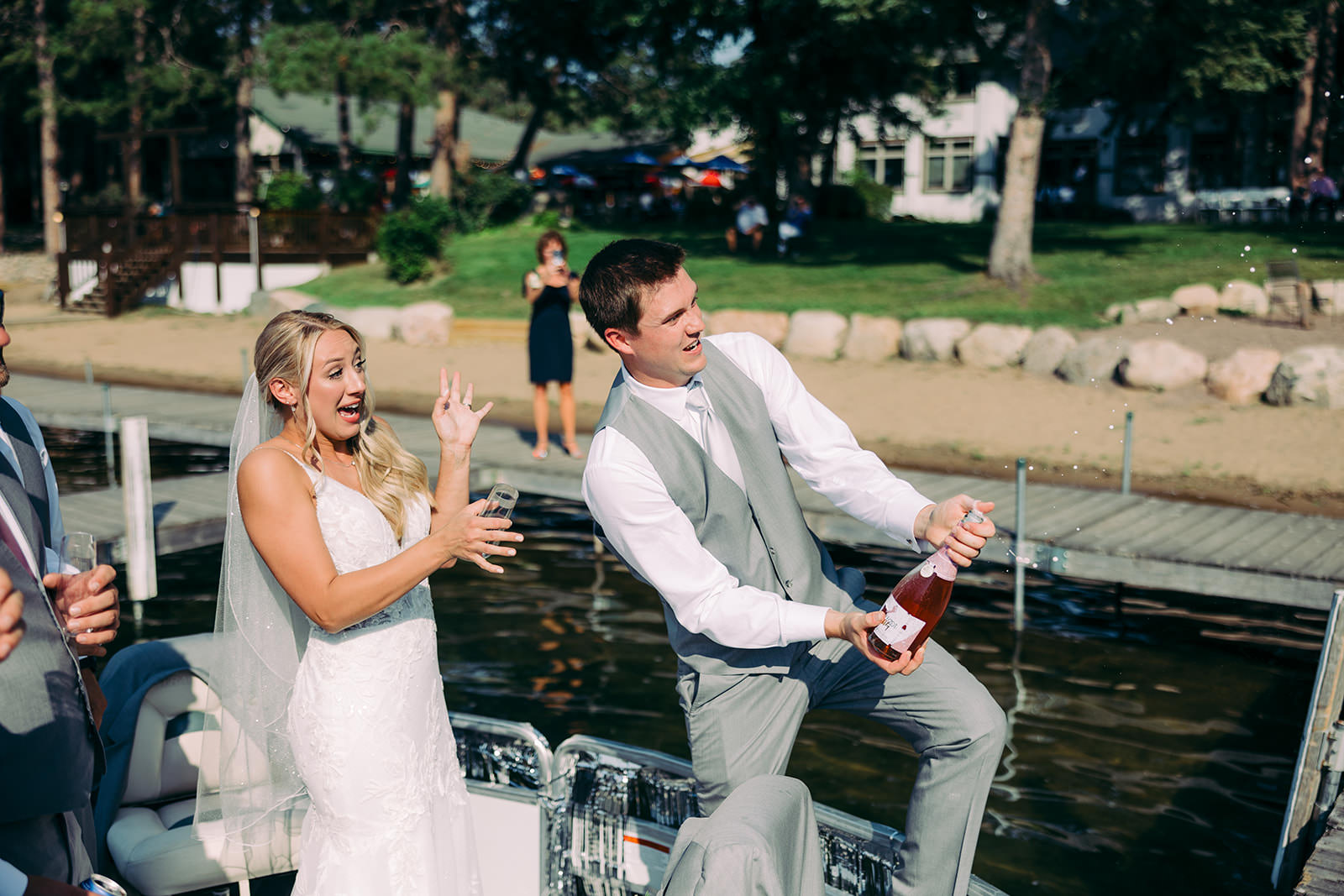 Couple popping champagne on the dock — bride laughing as it sprays — Tim Larsen Photography, Brainerd Lakes MN
