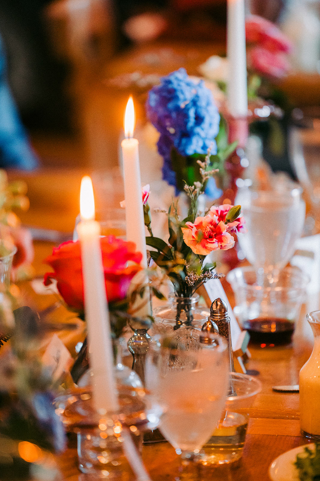 Reception table detail — taper candles, colorful flowers, and glassware in warm light — Tim Larsen Photography, Brainerd Lakes MN