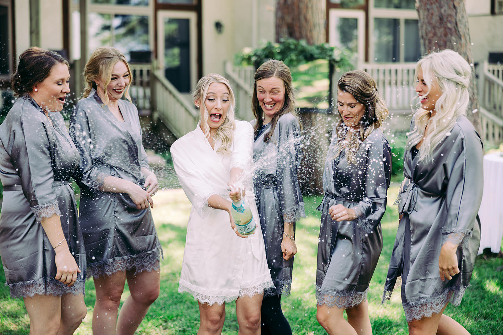 Bridesmaids popping champagne and laughing in gray robes on the lodge lawn — Tim Larsen Photography, Brainerd Lakes MN