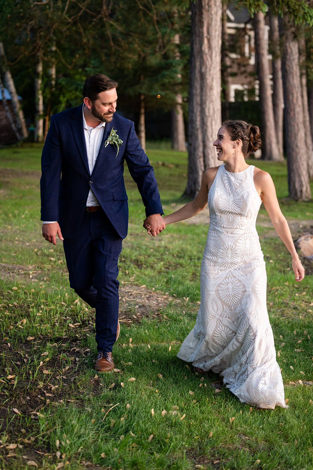 Couple walking through the pine trees on the lodge grounds — navy suit and geometric lace gown — Tim Larsen Photography, Brainerd Lakes MN