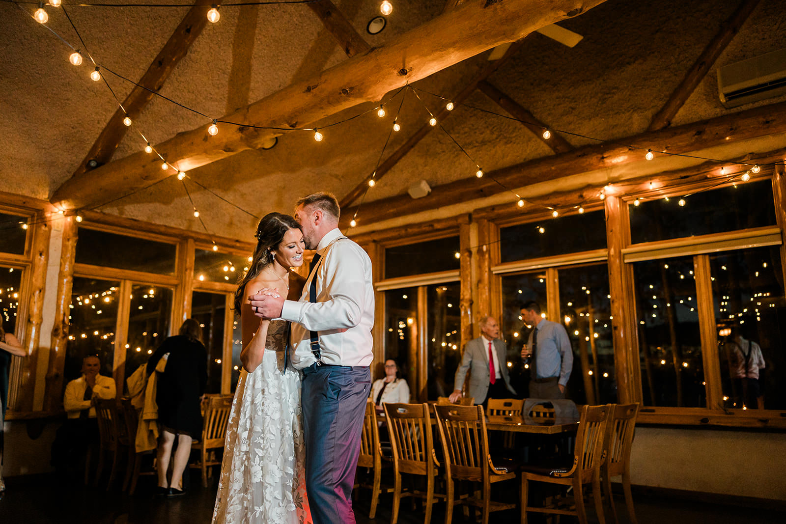 Couple kissing at the reception under string lights — timber and glass lodge room — Tim Larsen Photography, Brainerd Lakes MN