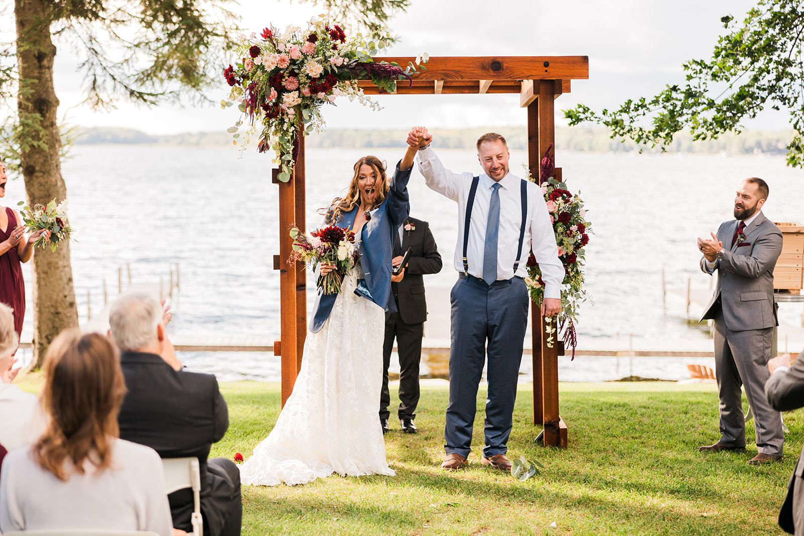 Couple raising hands after ceremony under wooden arbor with burgundy flowers — lakeside — Tim Larsen Photography, Brainerd Lakes MN