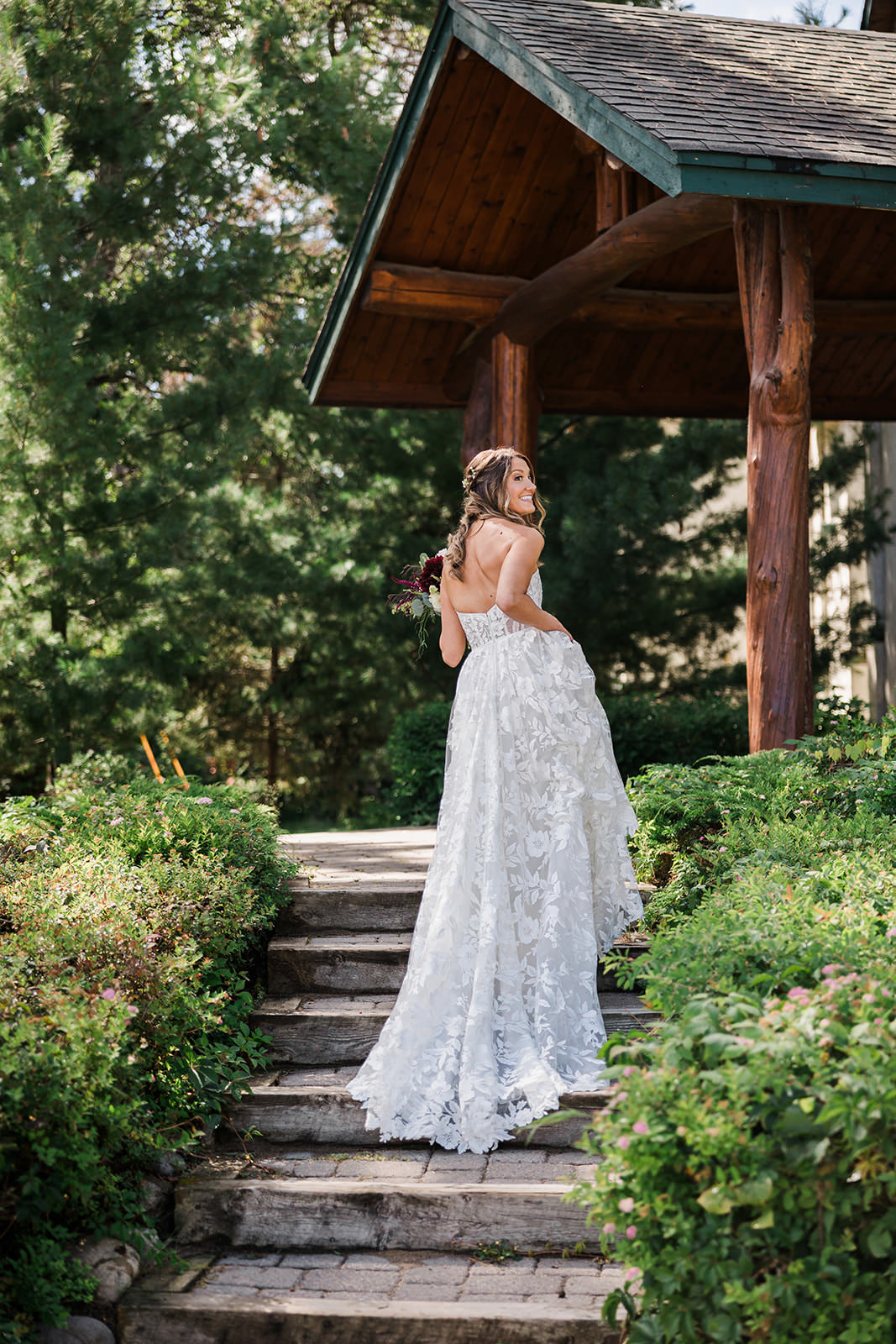Bride from behind walking up stone steps to the lodge gazebo — lace gown and bouquet — Tim Larsen Photography, Brainerd Lakes MN
