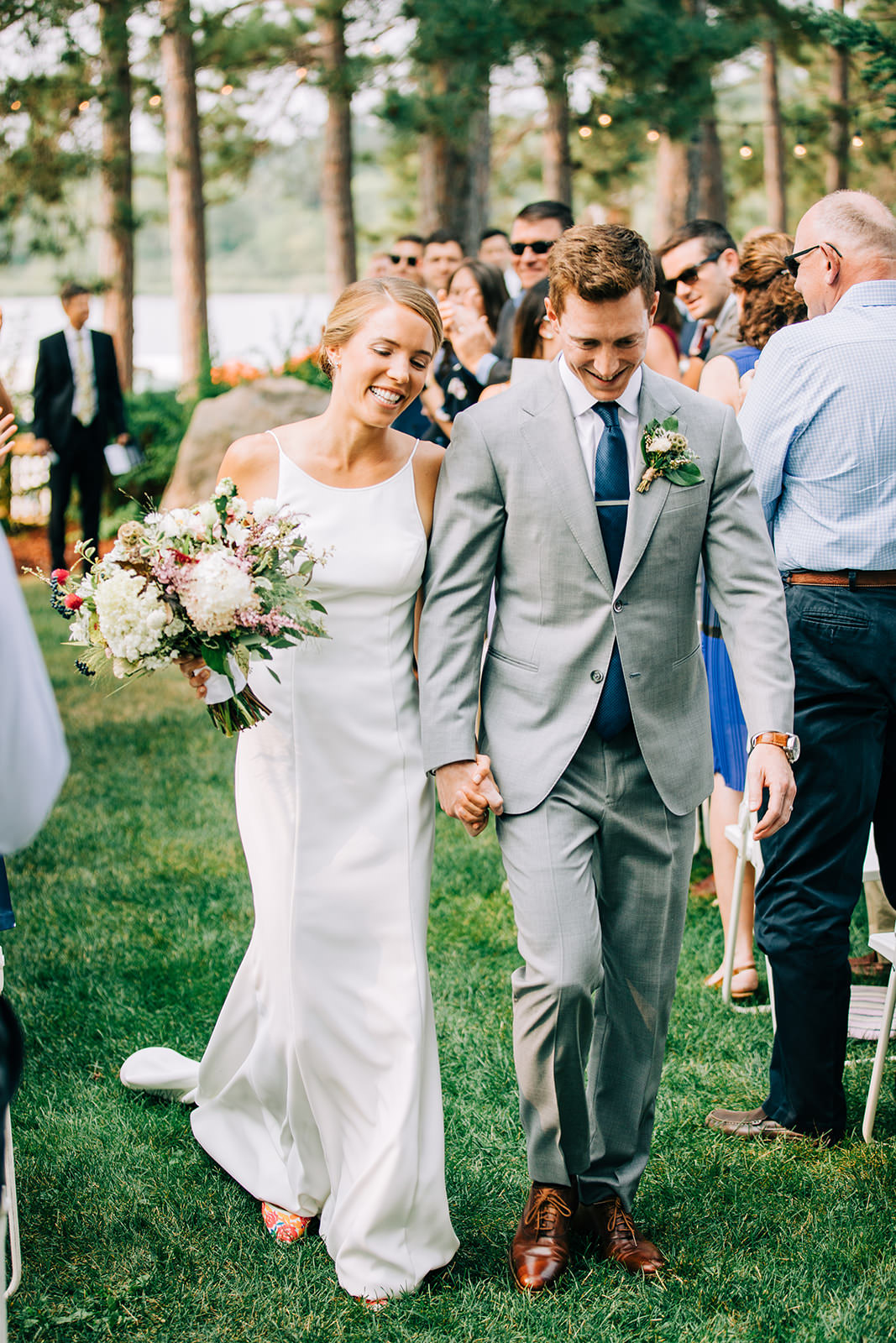 Couple laughing walking down the aisle — recessional on the lodge lawn — Tim Larsen Photography, Brainerd Lakes MN
