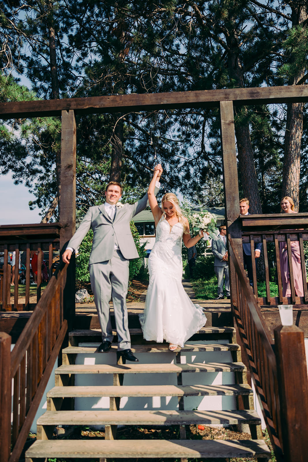 Couple raising hands walking down the wooden deck stairs after ceremony — Tim Larsen Photography, Brainerd Lakes MN