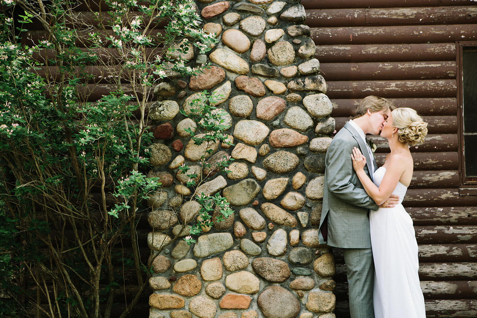 Couple kissing against the stone chimney and log wall at Manhattan Beach Lodge — Tim Larsen Photography, Brainerd Lakes MN