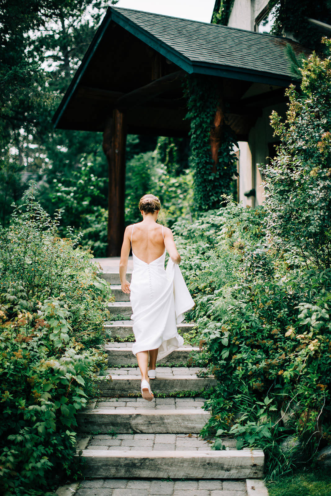 Bride walking up stone steps toward the lodge gazebo — back of lace gown — Tim Larsen Photography, Brainerd Lakes MN