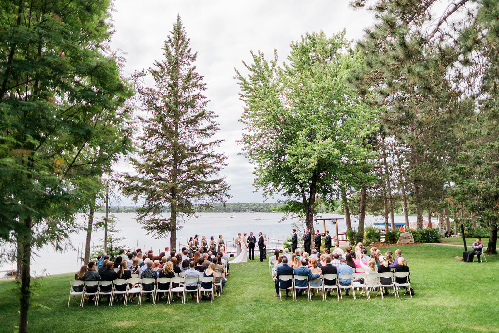 Wide outdoor ceremony on the lawn with tall pines and Big Trout Lake behind — Tim Larsen Photography, Brainerd Lakes MN