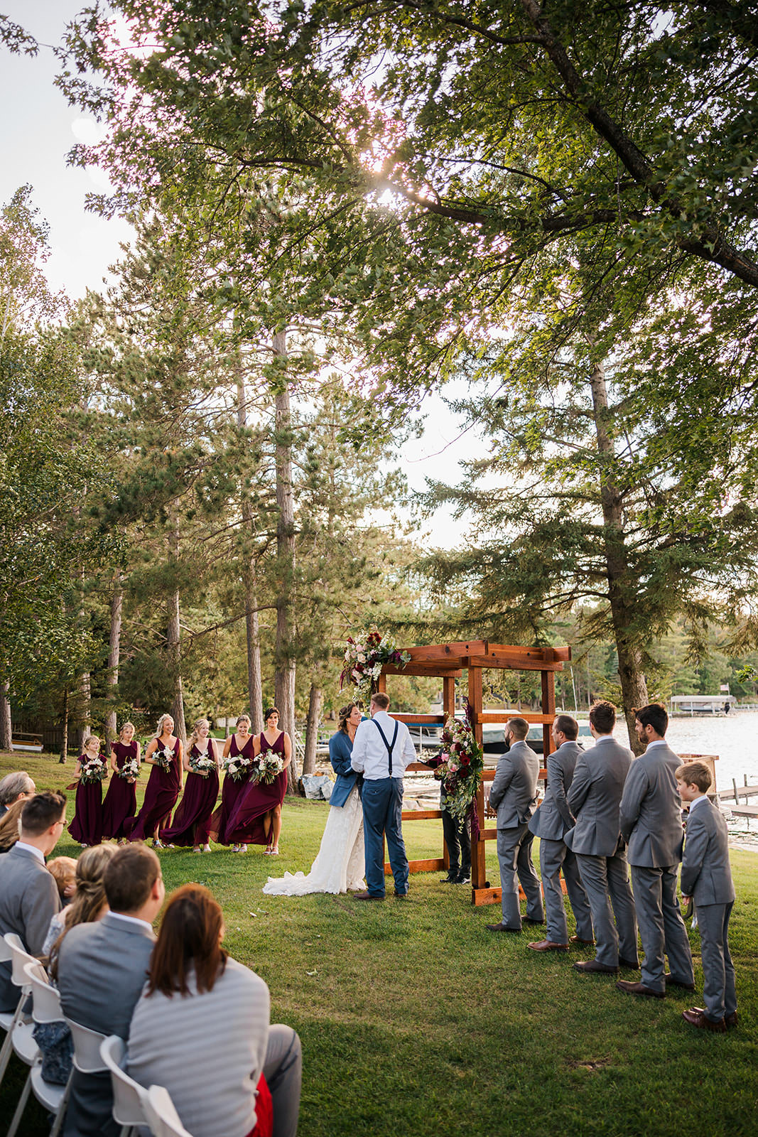 Ceremony under wooden arbor at sunset with burgundy wedding party — pine trees and lake — Tim Larsen Photography, Brainerd Lakes MN