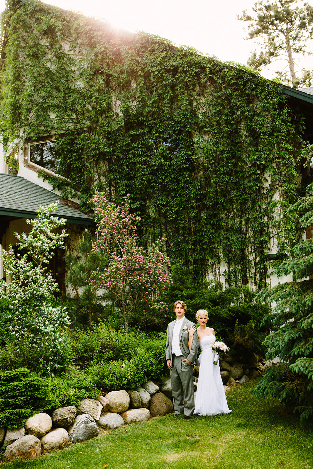 Couple in front of the ivy-covered lodge — bride with short hair and white bouquet — Tim Larsen Photography, Brainerd Lakes MN