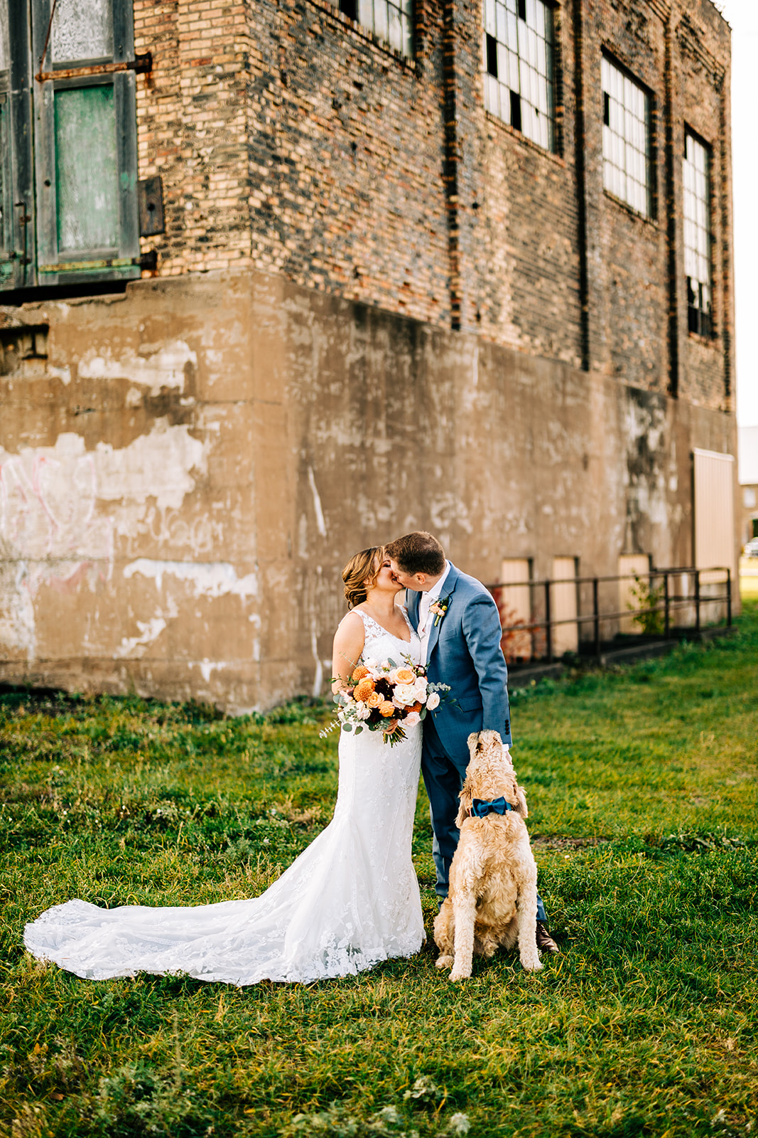 Couple kissing with dog on the green lawn outside the industrial building — Tim Larsen Photography, Brainerd Lakes MN