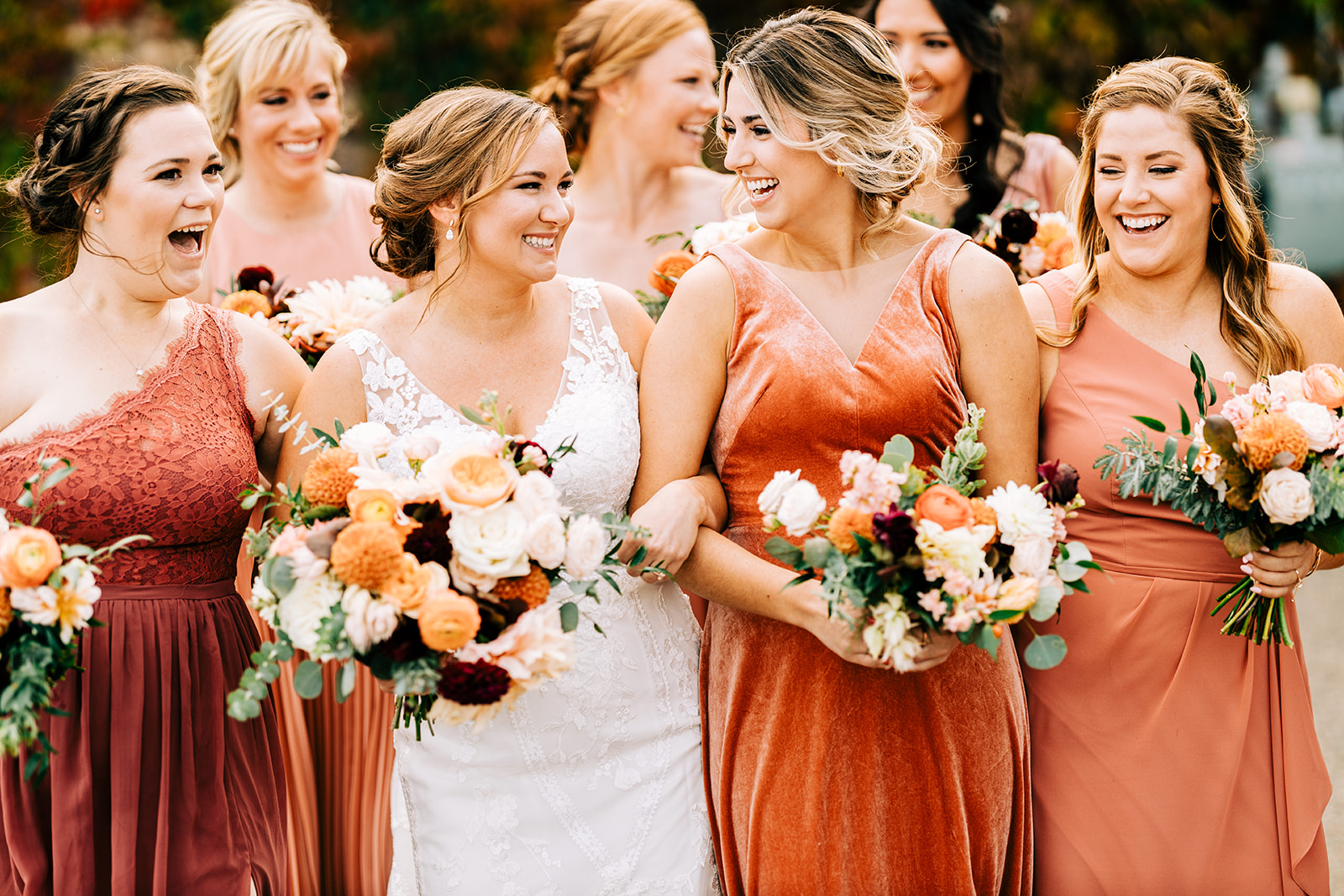 Bride laughing with bridesmaids in mismatched rust and copper dresses — fall bouquets — Tim Larsen Photography, Brainerd Lakes MN