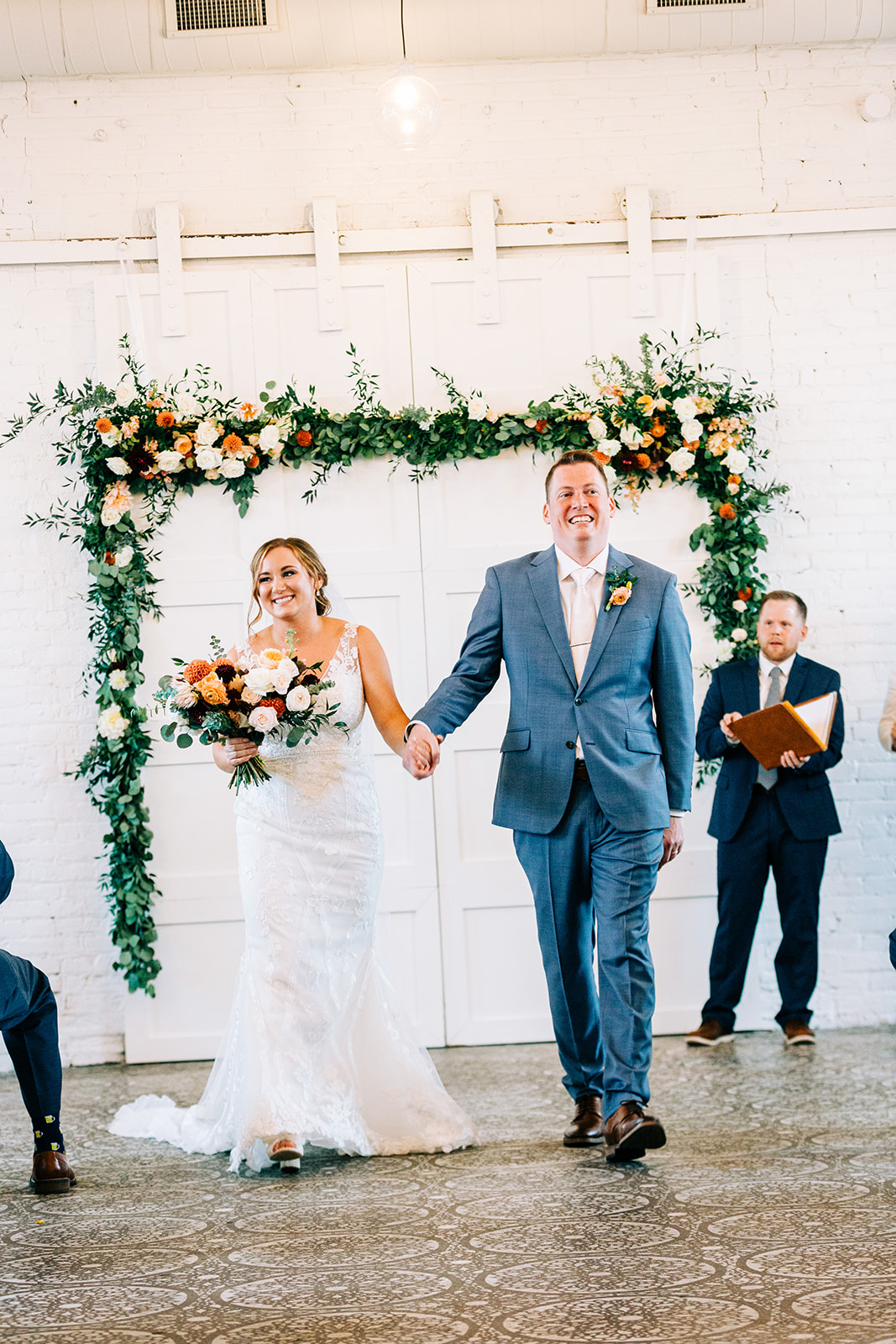Couple recessional under greenery arch in the white room — orange and peach bouquet — Tim Larsen Photography, Brainerd Lakes MN